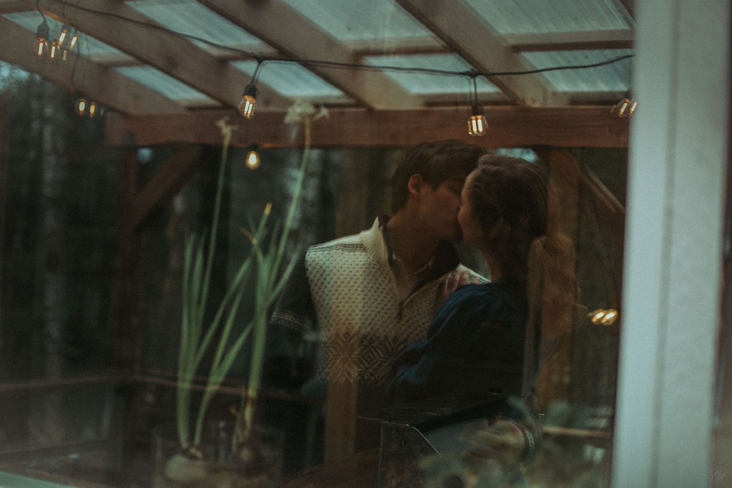 A romantic couple shares an intimate moment viewed through glass with green plants in the background in Southeast Alaska.