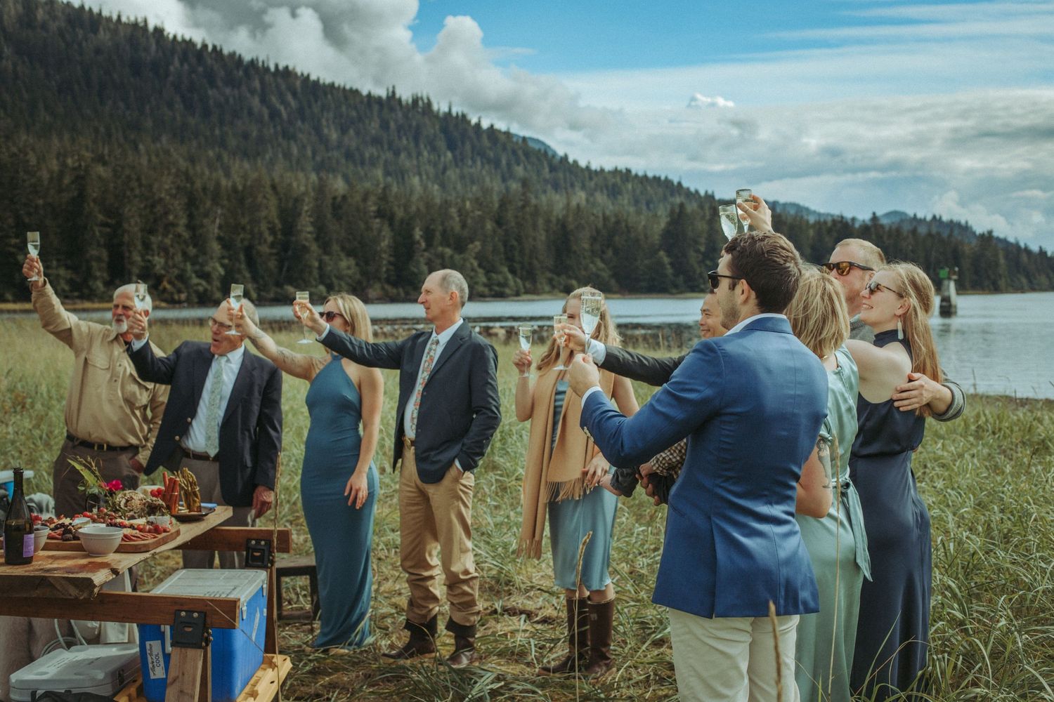 Guests celebrating at an outdoor wedding reception with mountains and lake in the background in Alaska.