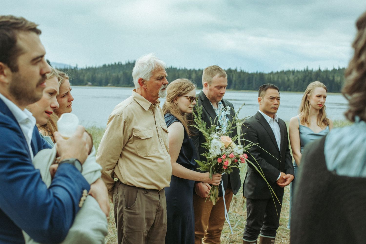 Small wedding gathering stands together during an overcast outdoor ceremony in Alaska.