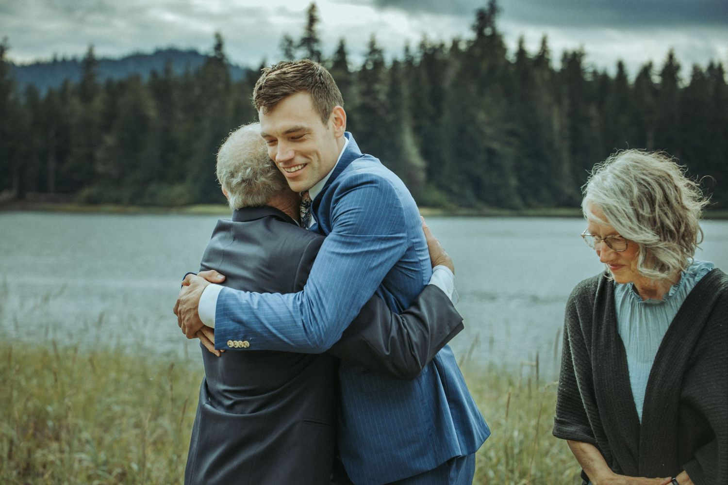 Emotional embraces shared during an outdoor gathering by a scenic mountain lake.