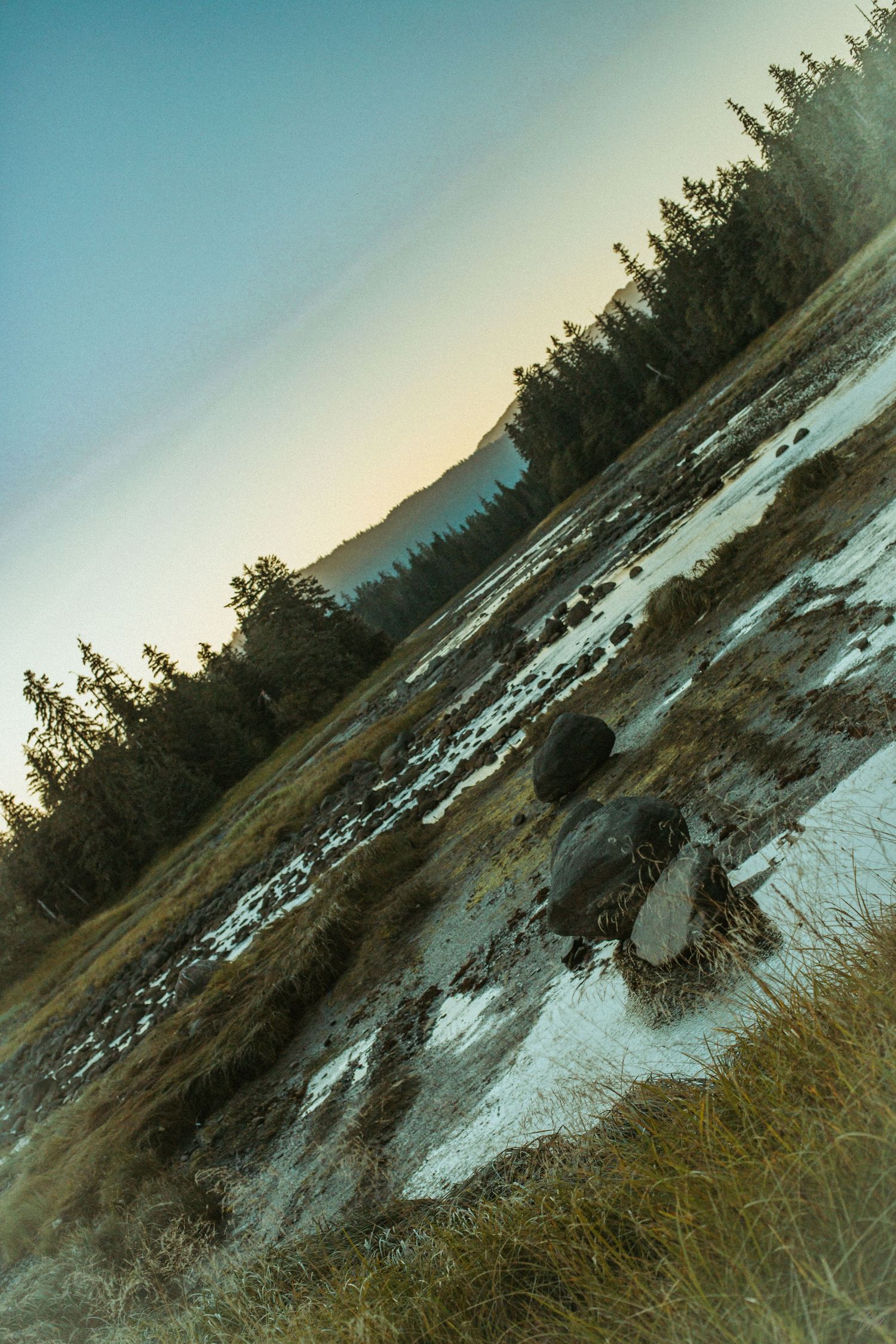 Tilted landscape view of mountain lake with patches of snow at sunset.