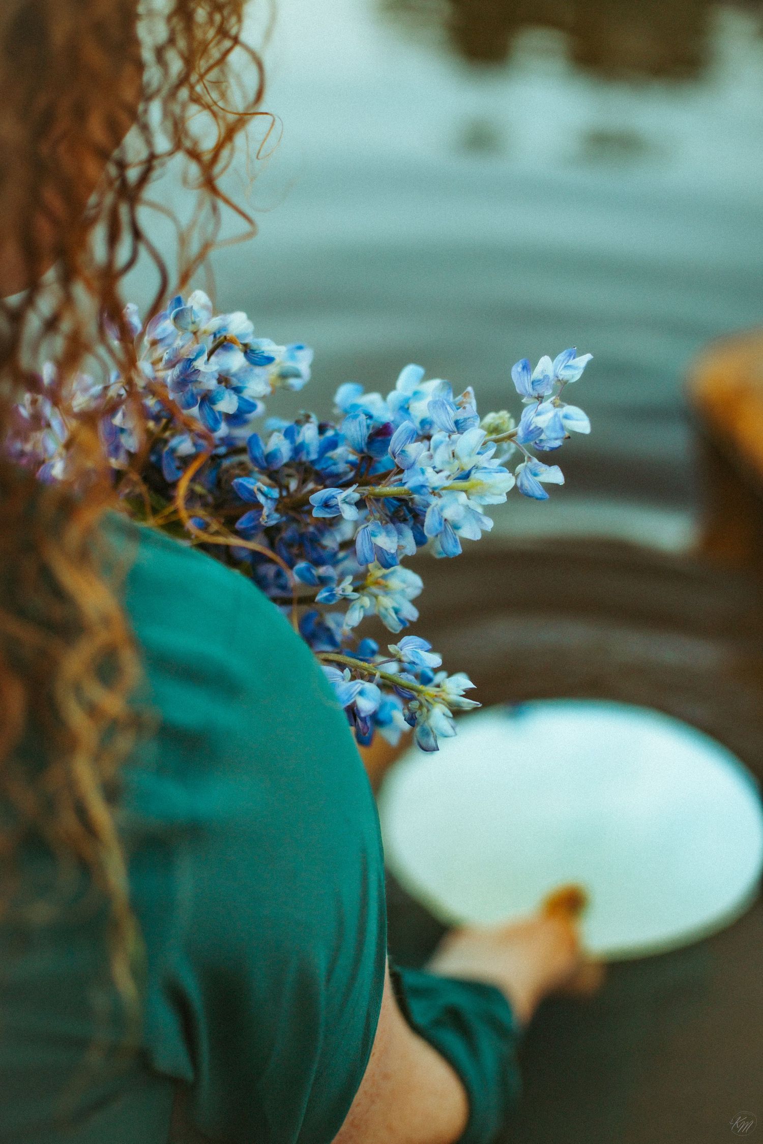Close-up of blue delphinium flowers against teal fabric with mirror reflection.