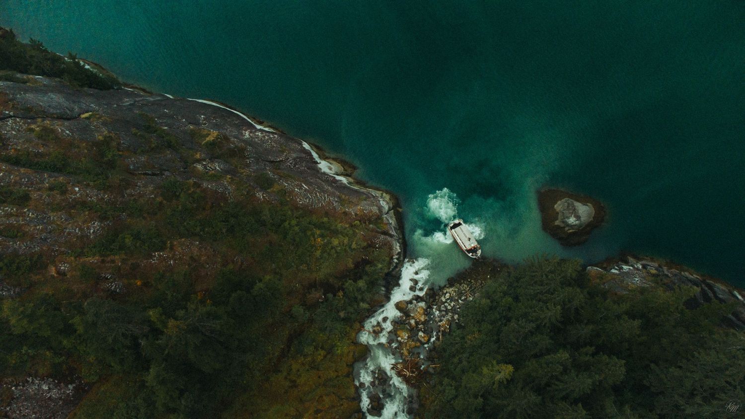 Aerial view of a cascading waterfall flowing into a turquoise fjord surrounded by lush green rocky cliffs.