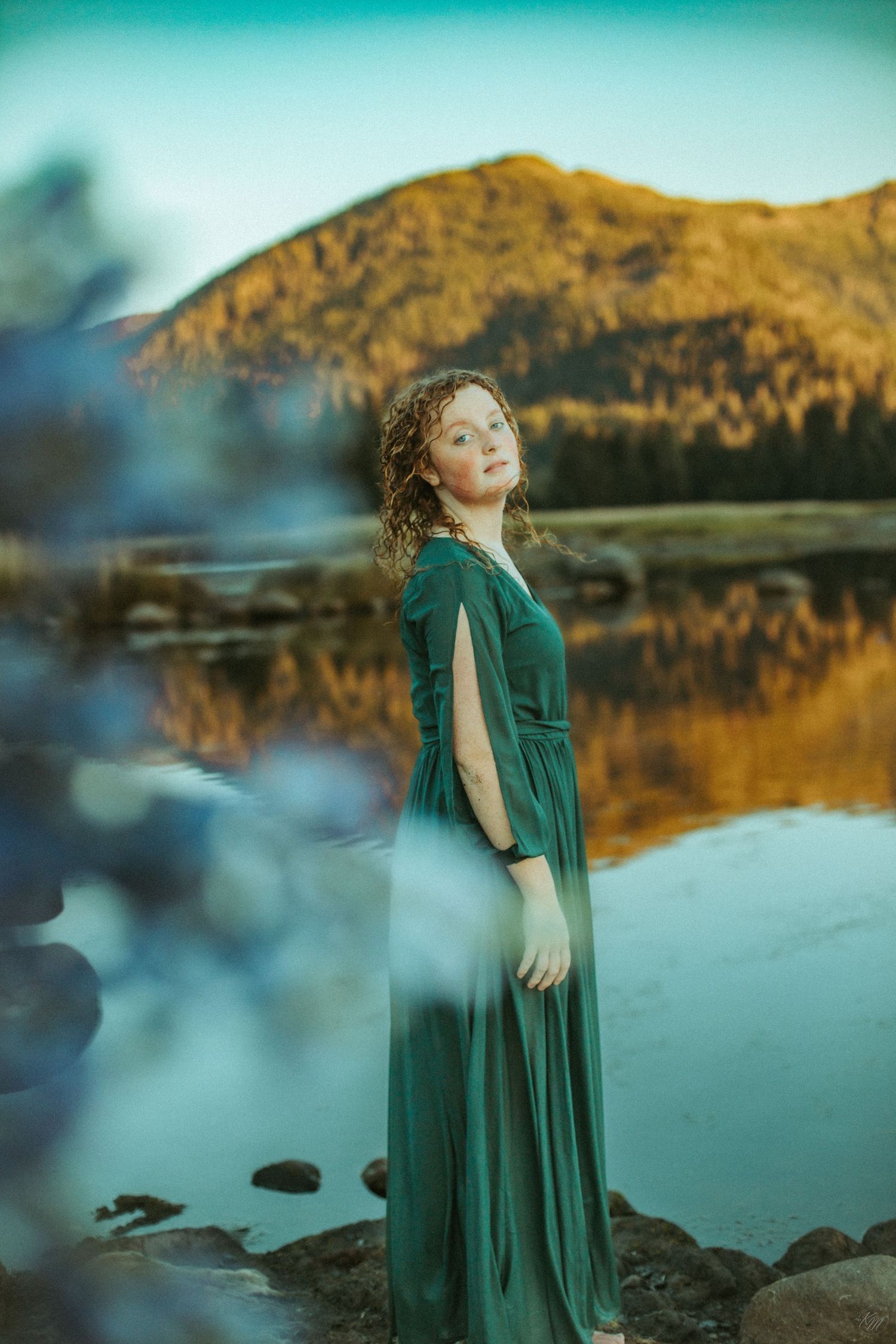 Emerald dress silhouette against mountain lake reflection at dusk.