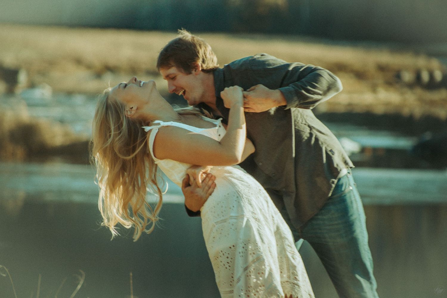 A romantic couple in casual clothes embrace in a graceful dip pose against a blurred outdoor background at sunset in Southeast Alaska.
