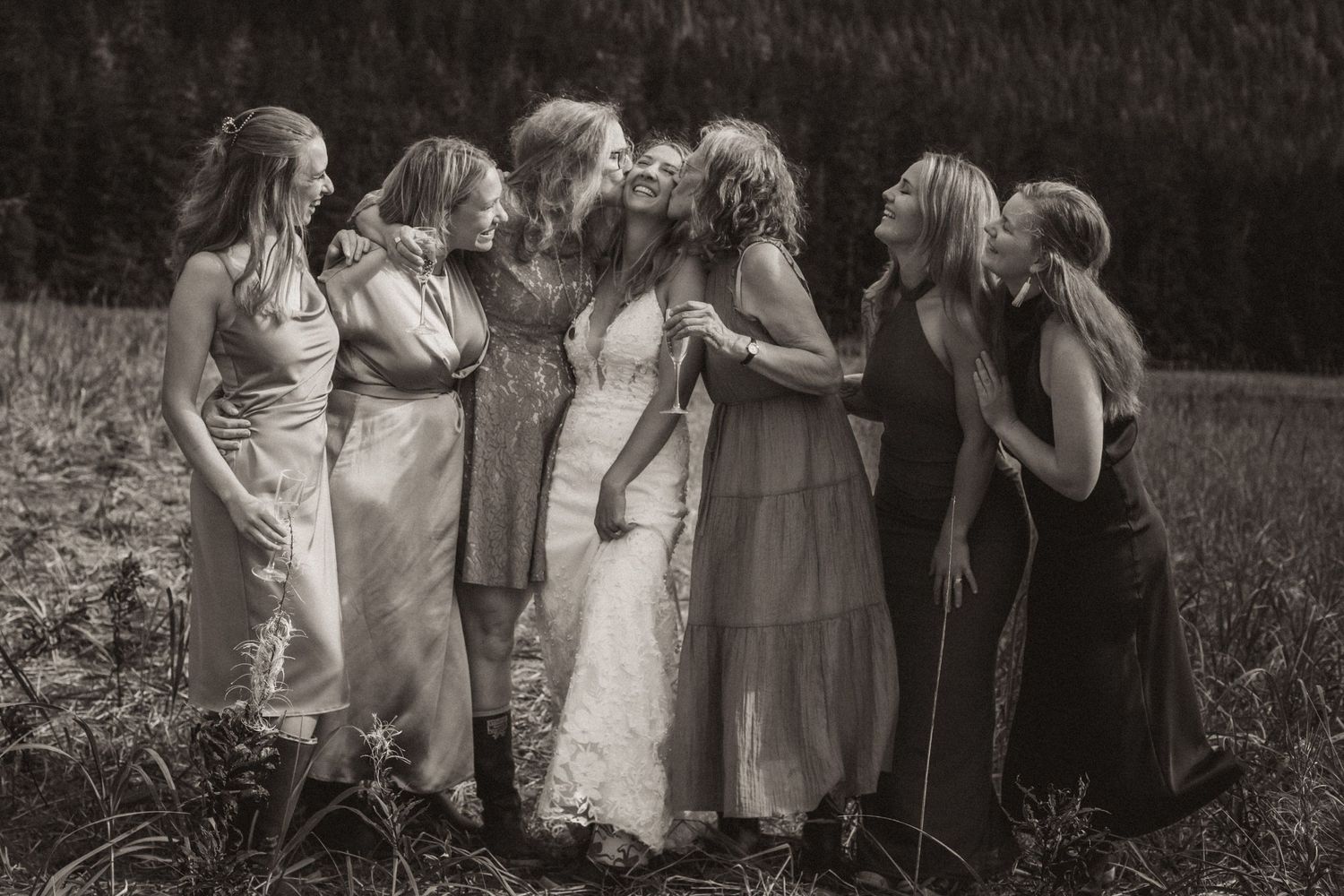 Intimate group of bridesmaids in flowing dresses share a moment in black and white photography.