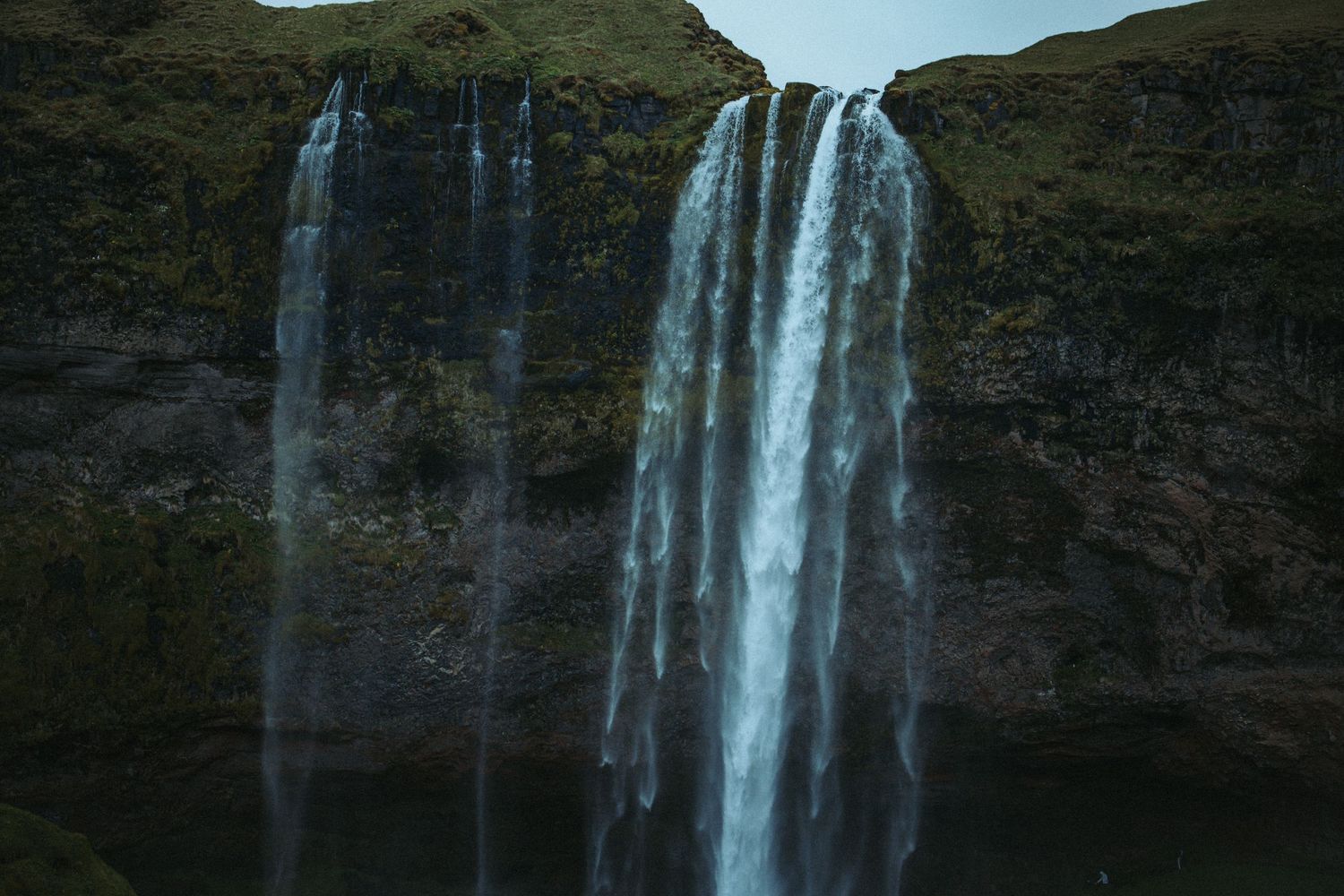 Majestic Seljalandsfoss waterfall cascading down mossy cliffs in Iceland under overcast skies.