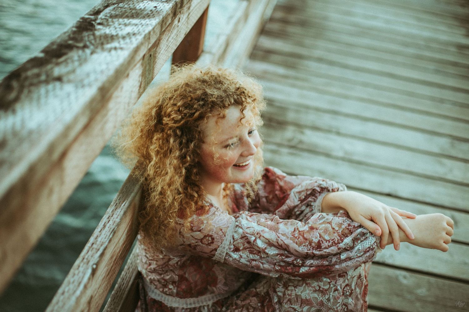 Candid moment on wooden dock with flowing dress and curls.