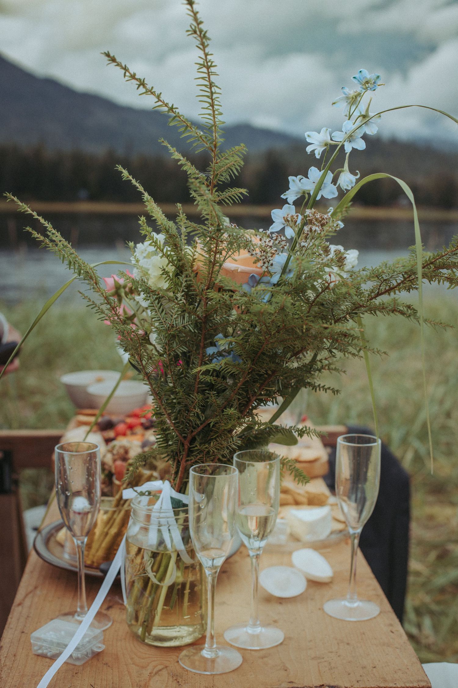 Rustic wedding reception table with wildflower centerpiece and champagne glasses by a lake in Alaska.