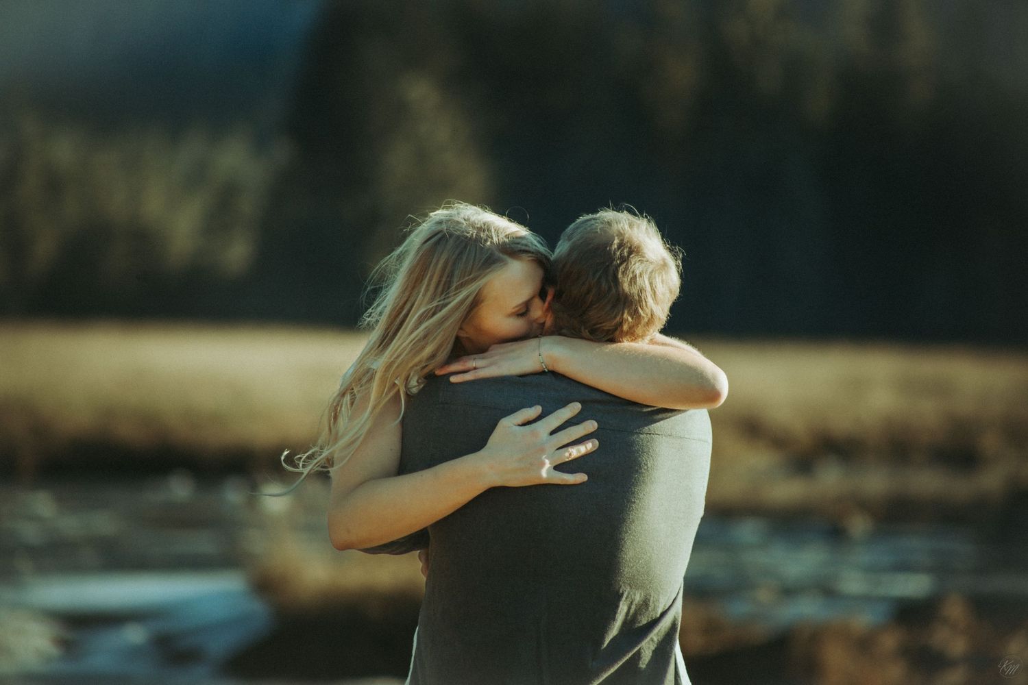 Two people share an intimate embrace near a serene waterfront during golden hour in Southeast Alaska.