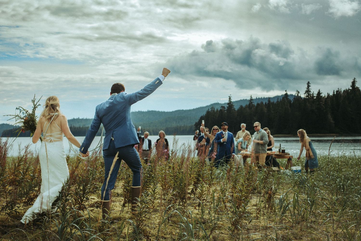 Wedding celebration in a scenic mountain field with guests following the newlyweds in Alaska.