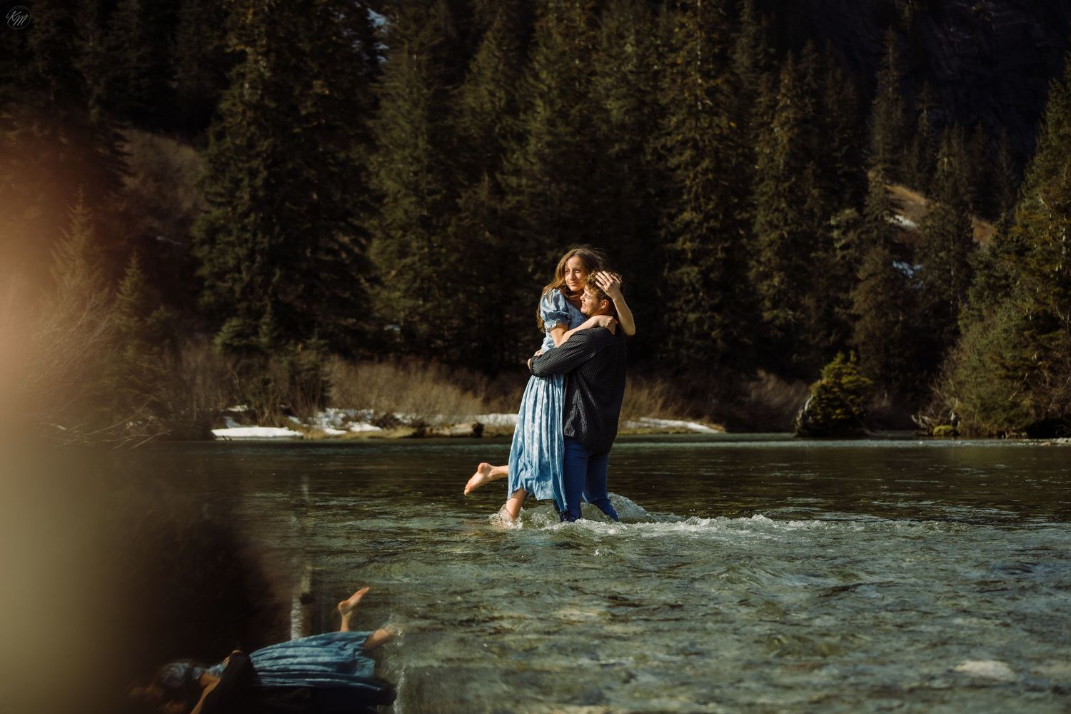 Scenic mountain engagement session by rushing river with evergreen forest backdrop.
