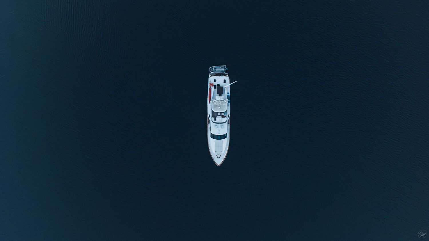Aerial top-down view of a white luxury yacht sailing on dark blue ocean waters at night.