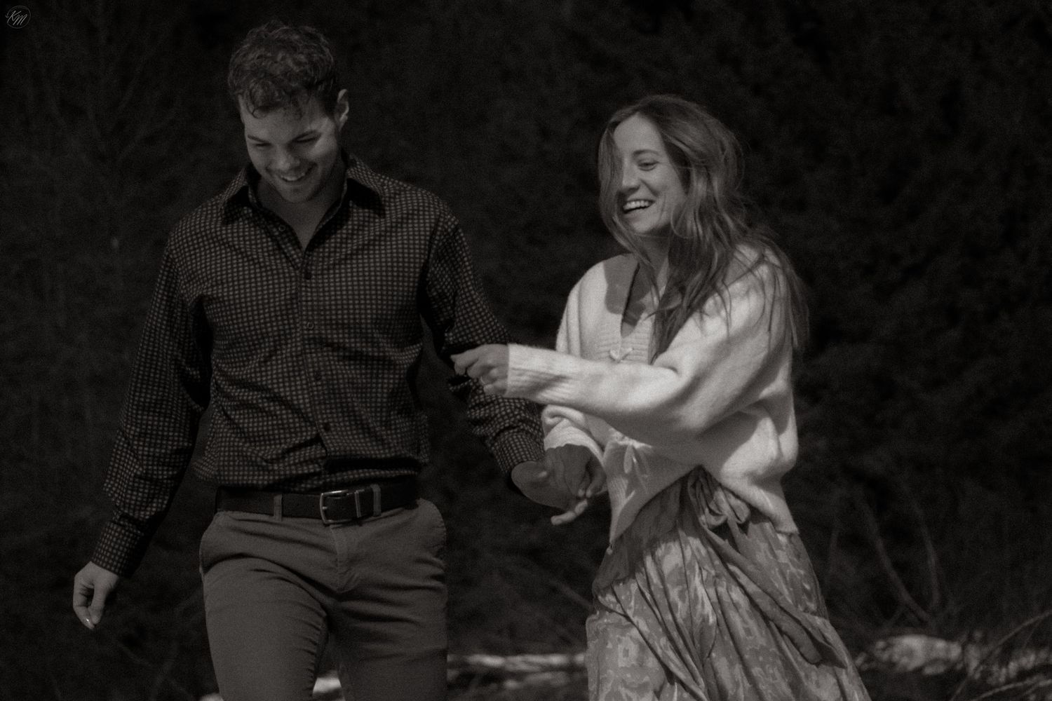 Candid black and white photo of couple dancing and laughing together outdoors.