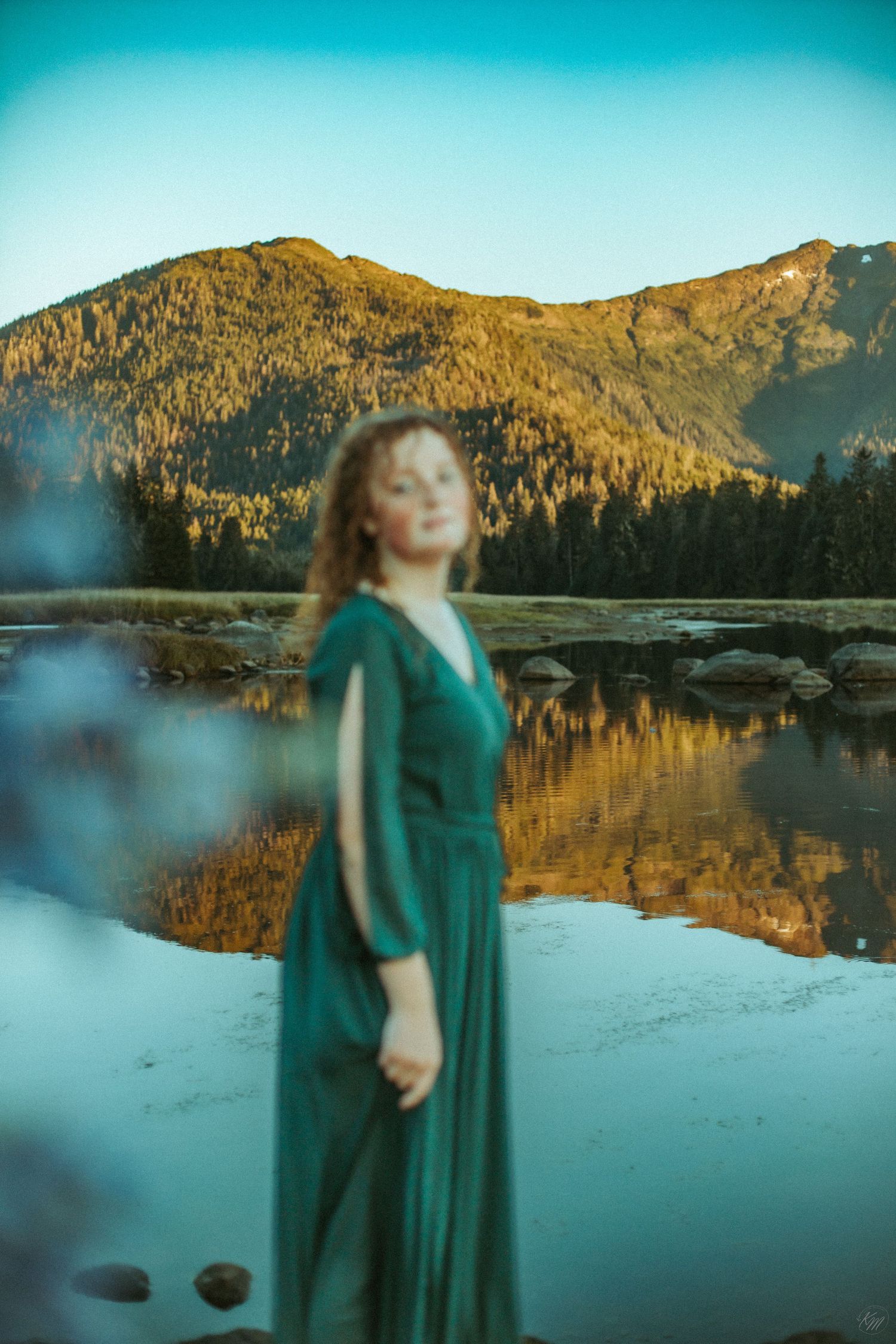 Scenic mountain landscape reflected in still waters with figure in green dress.