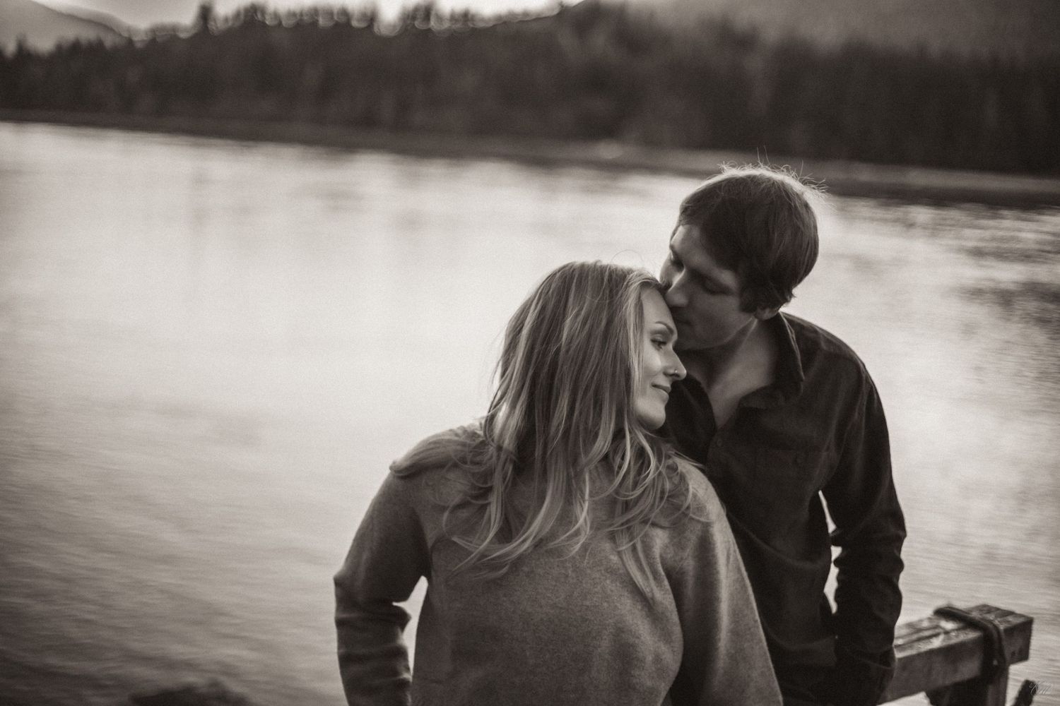 A romantic black and white photo of a couple sharing a tender moment by a serene lake in Southeast Alaska