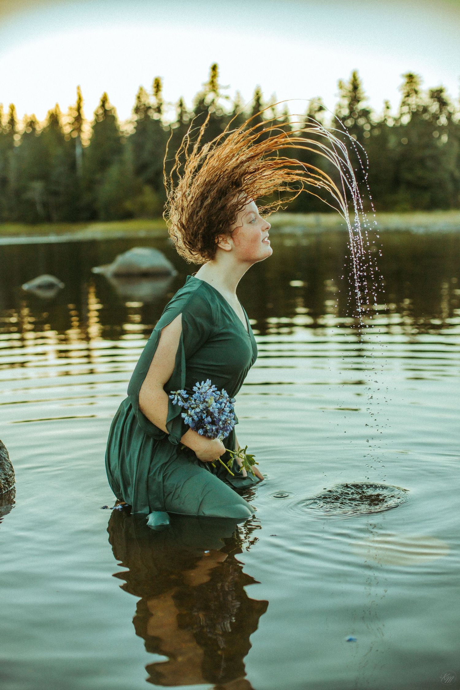 Dynamic water splash photo with hair movement and blue flowers by lake.