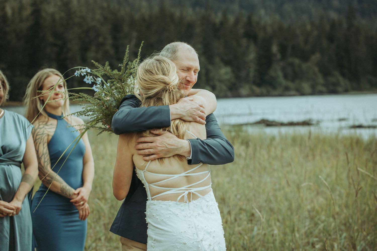 Group shares embraces during emotional outdoor ceremony by scenic mountain lake in Alaska.