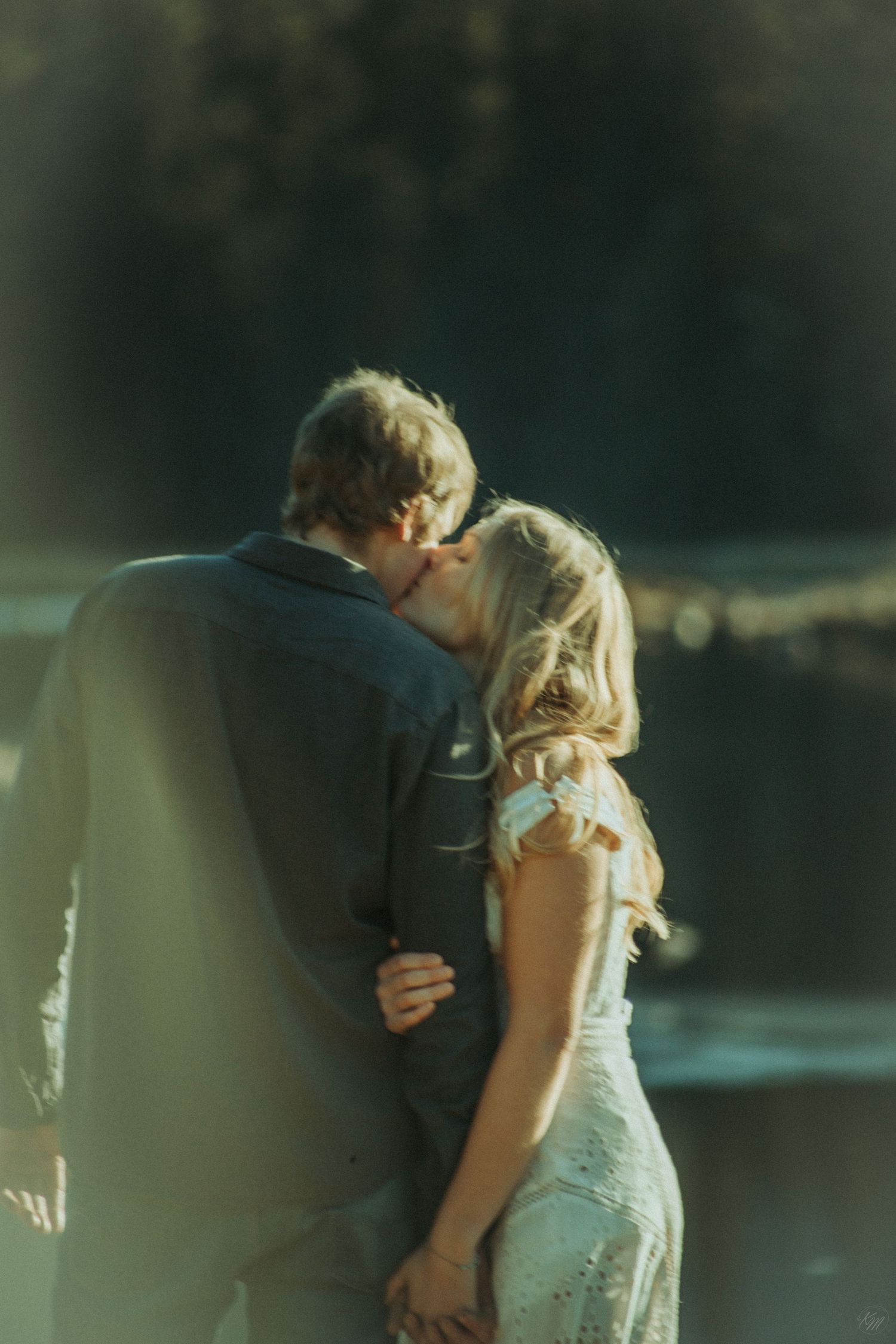 A romantic couple share an intimate moment by a tranquil lake, the bride in white and groom in dark sweater in Southeast Alaska.
