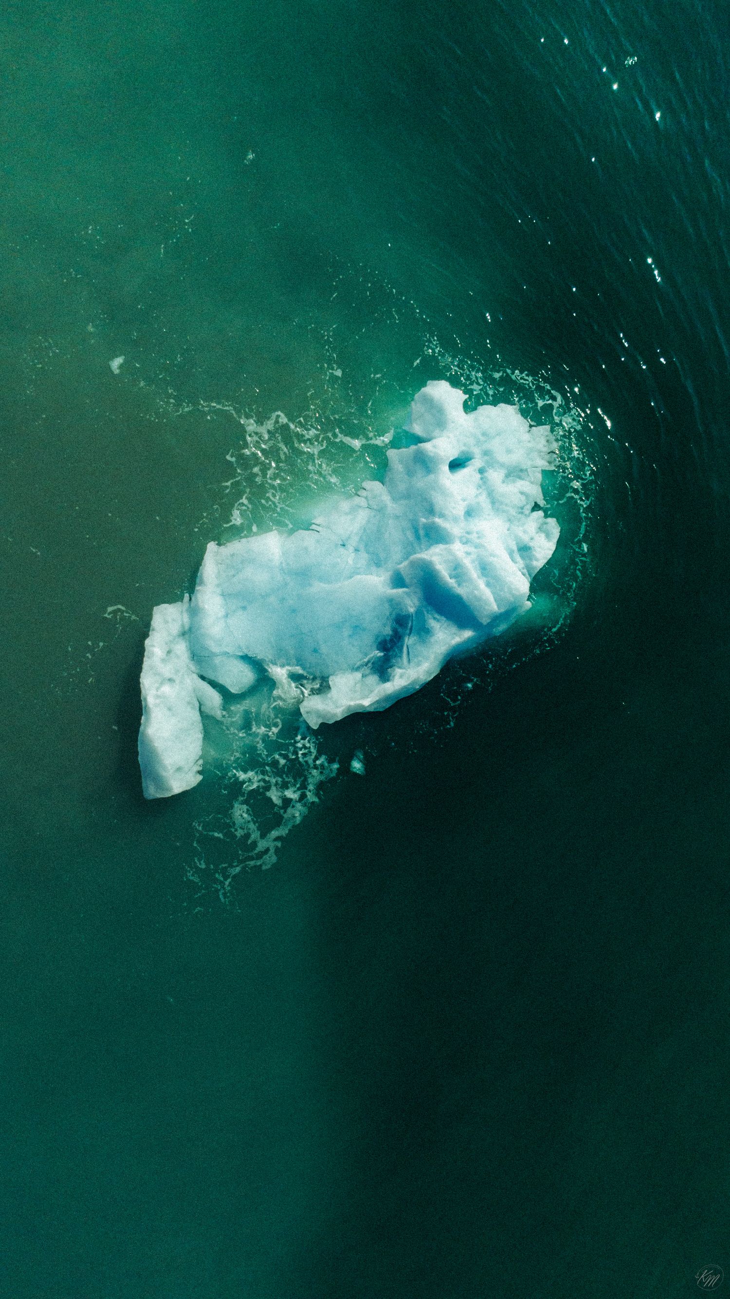 Aerial drone shot of a lone ice chunk floating in deep green ocean waters.