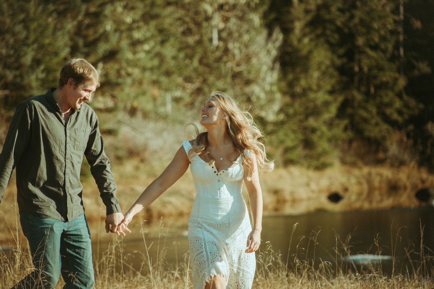 A couple holds hands while walking through a sunlit meadow near a lake on a warm autumn day in Southeast Alaska.