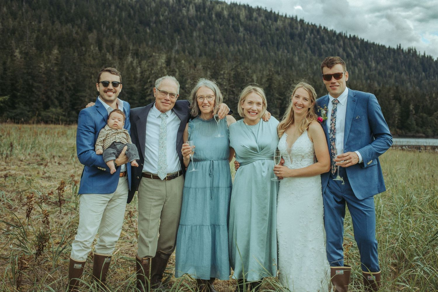 Wedding party group photo in blue and white attire against a mountainous landscape.