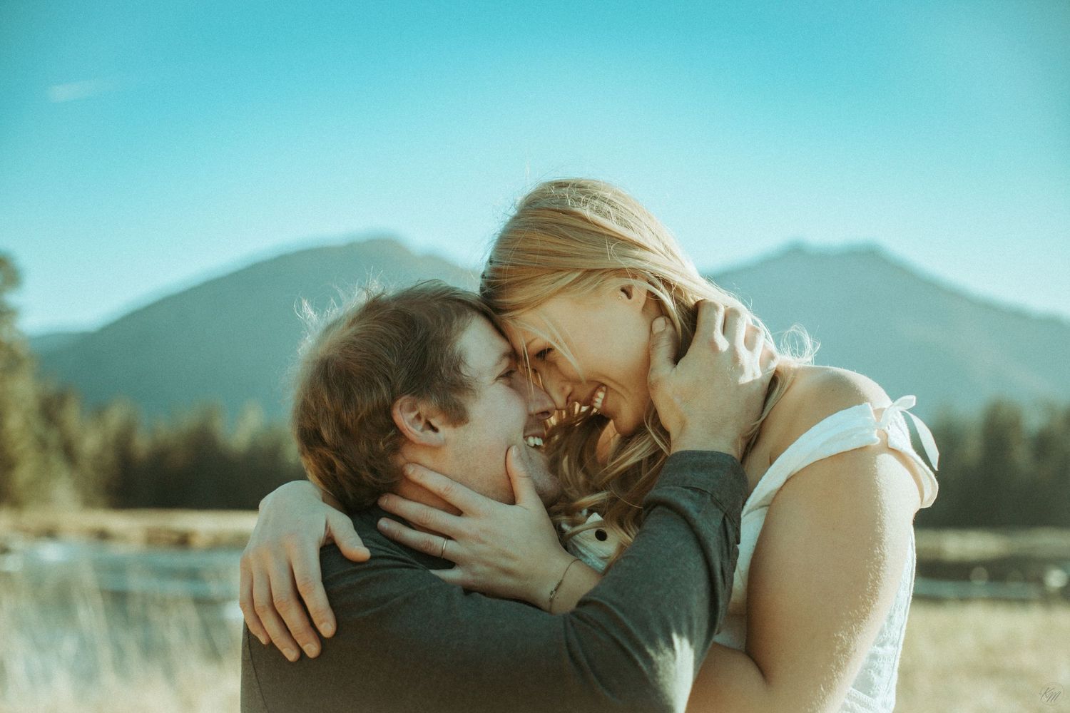 A close up of a couple embracing in a golden meadow with majestic mountains and evergreen forest in the background in Southeast Alaska
