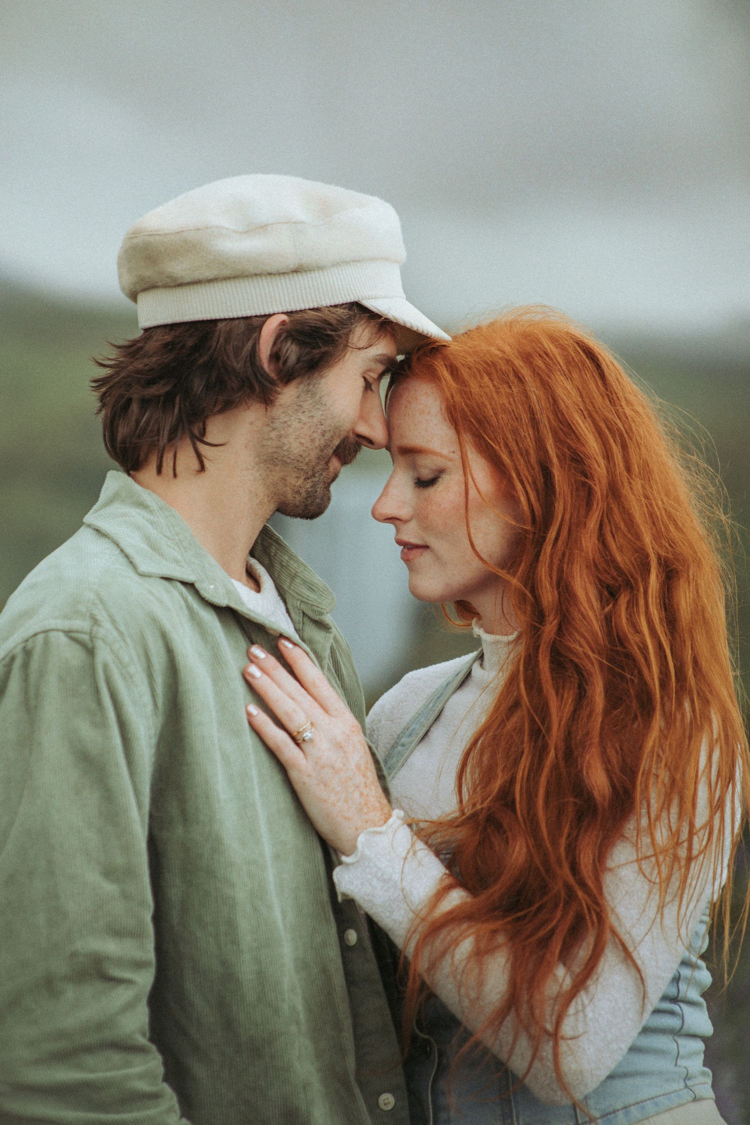 Romantic couple touching foreheads tenderly outdoors, woman with long red hair placing hand on mans chest.