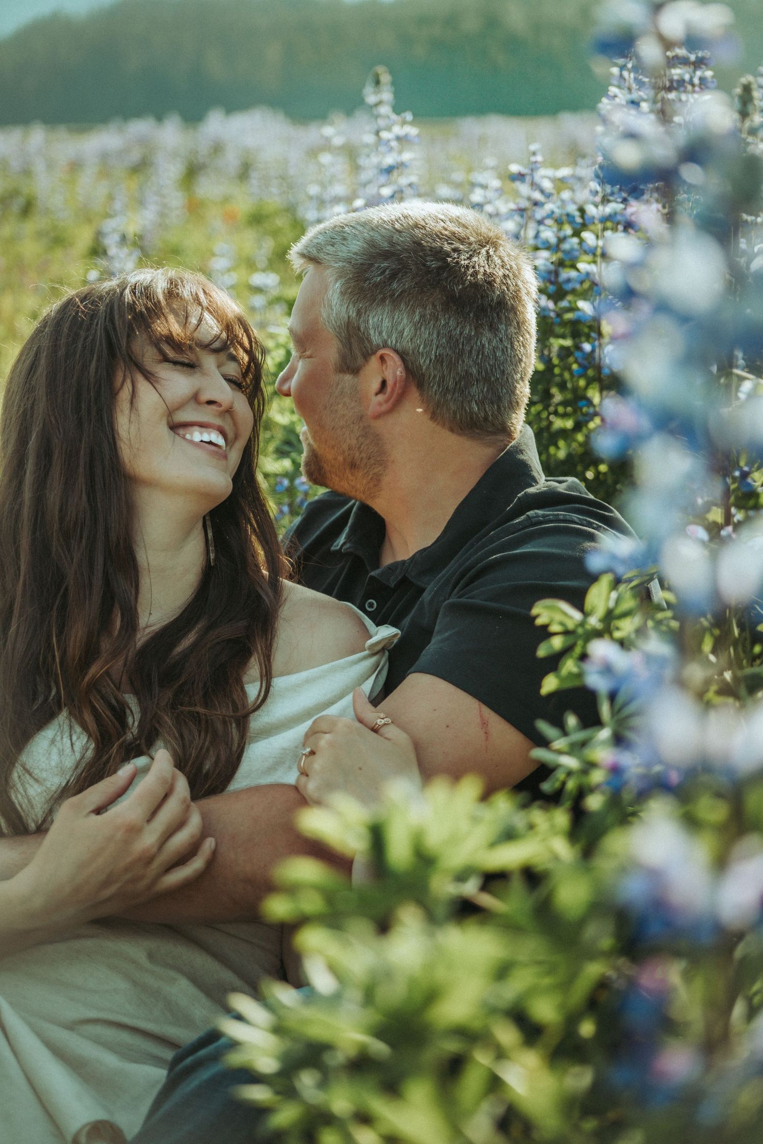 A romantic couple shares a tender moment sitting among blooming blue lupines in a sunny meadow in Southeast Alaska..