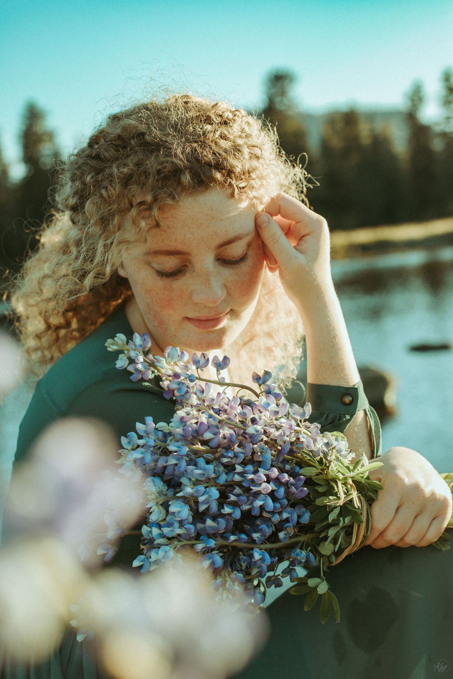 Romantic portrait holding blue wildflowers by a serene lake.
