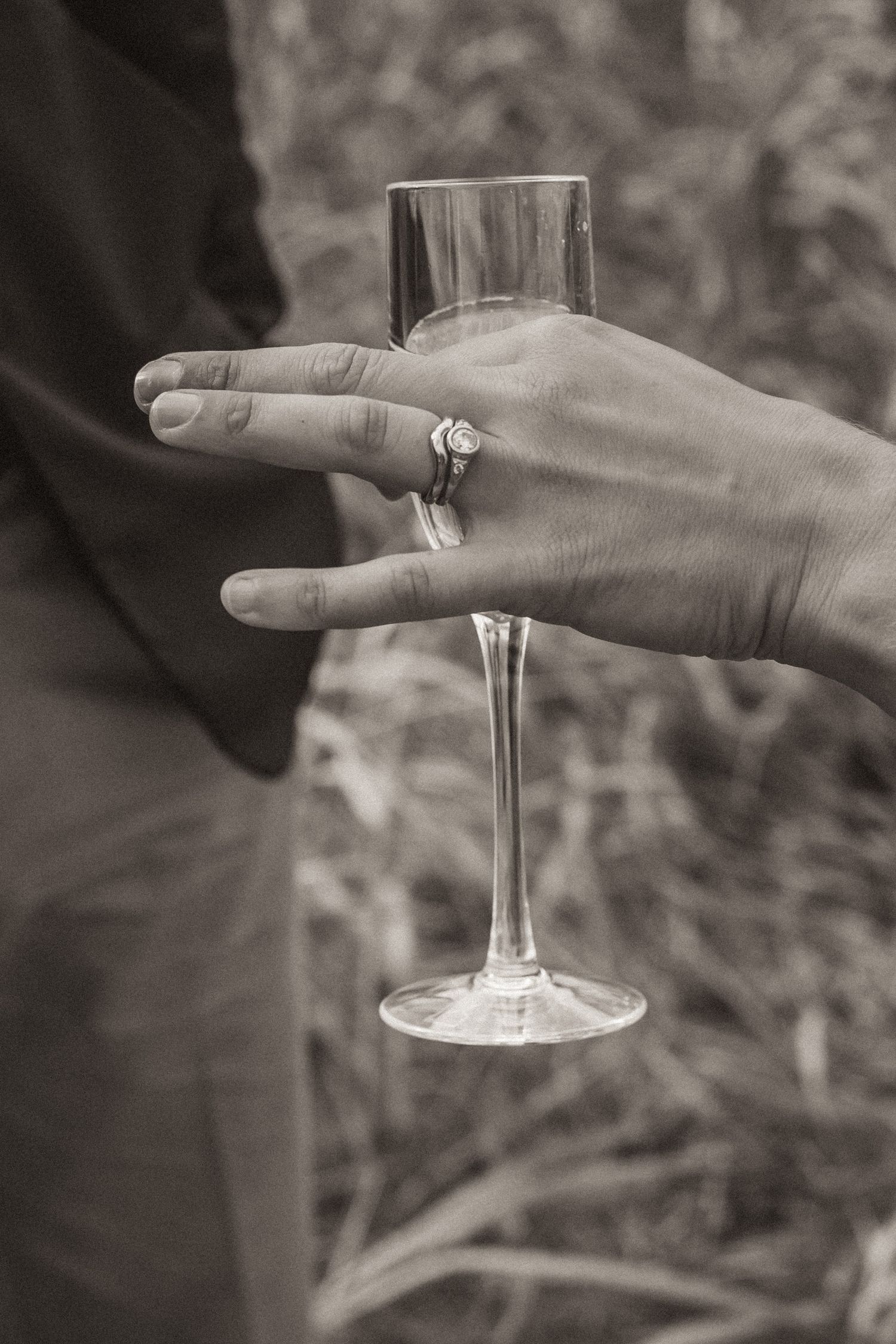 Hand holding champagne glass displays engagement ring in black and white photography.