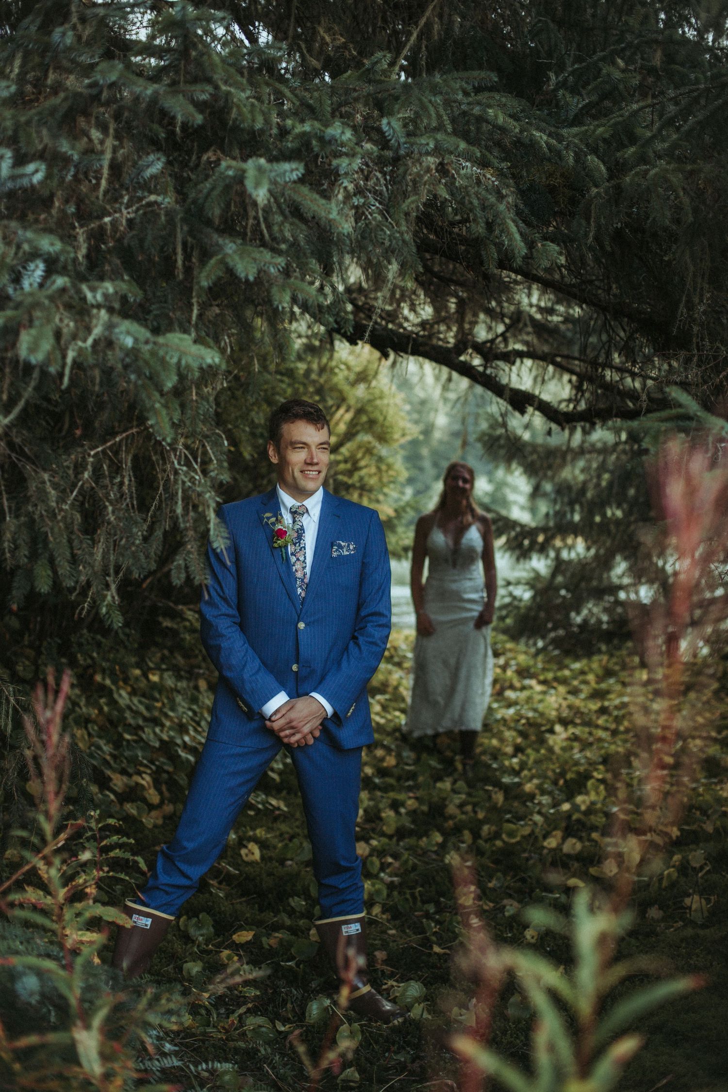 A person in a blue suit stands in a wooded forest setting with ethereal lighting.