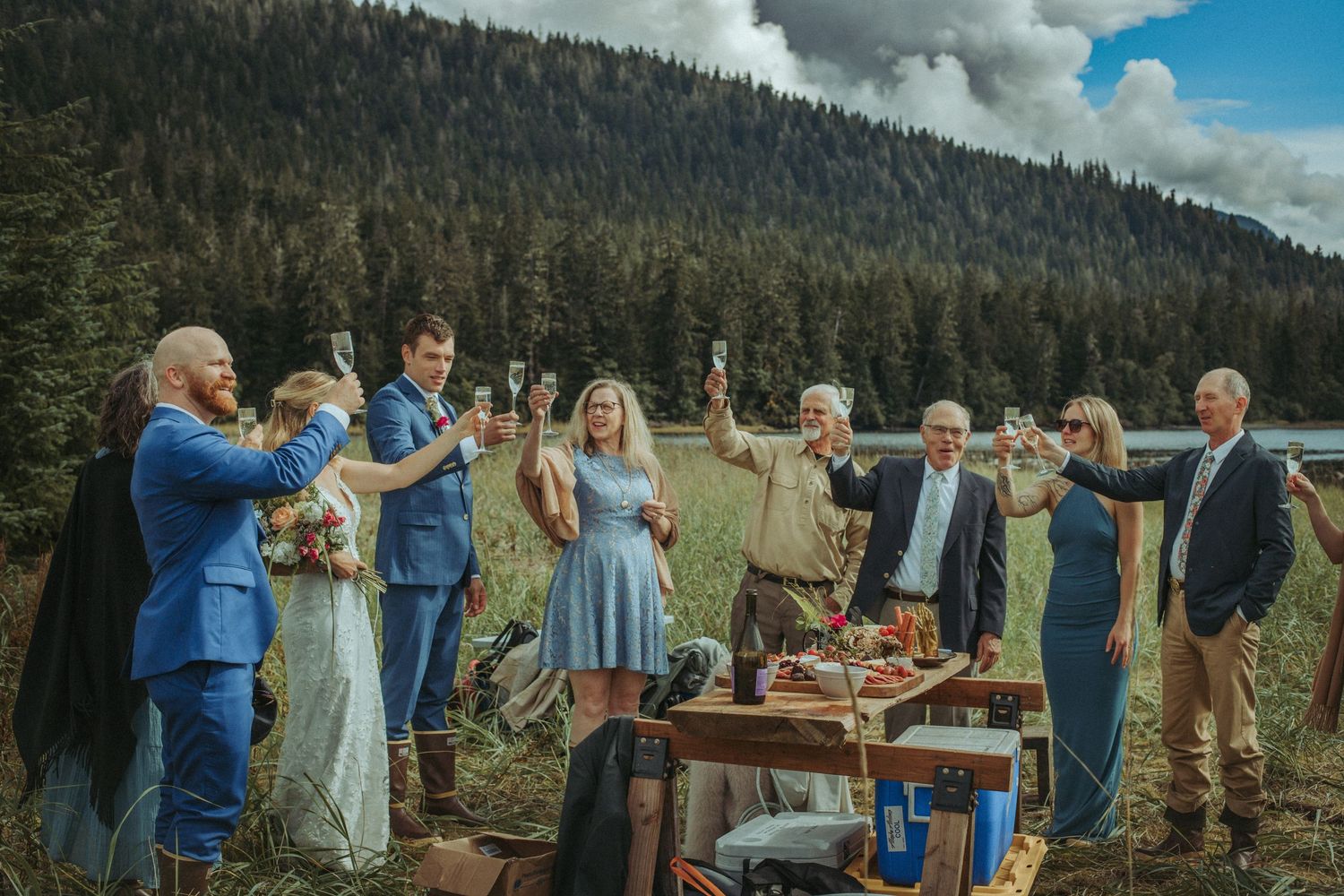 Wedding party toasting outdoors with a scenic mountain backdrop and rustic table setting in Alaska.