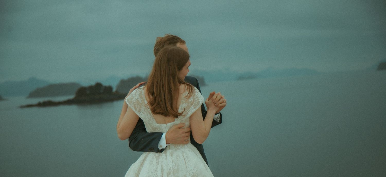 Bride and Groom embracing while overlooking a dramatic misty ocean landscape with rocky islands in Southeast Alaska.