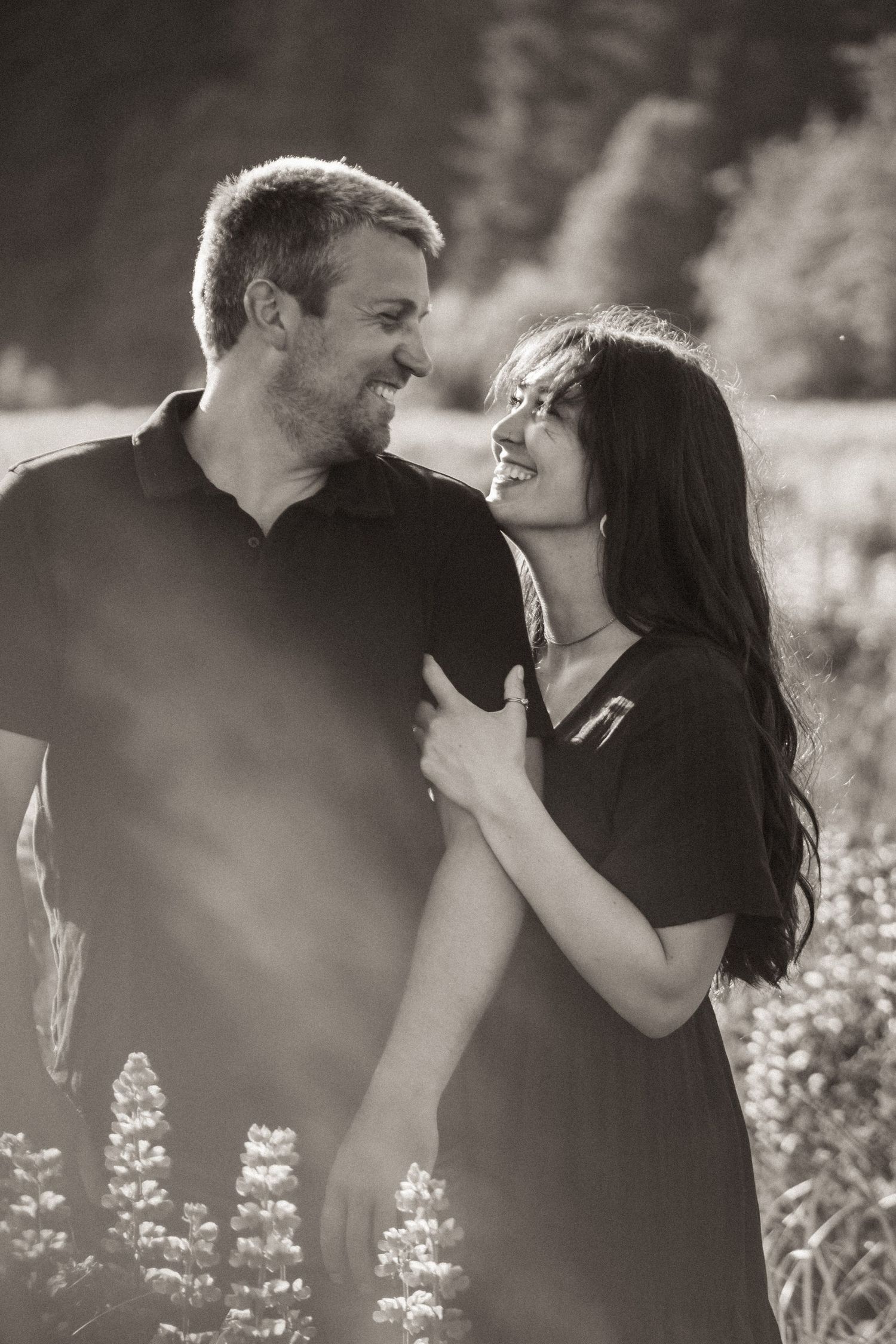 A romantic black and white portrait of a couple laughing together in a field of wildflowers on a sunny day in Alaska.