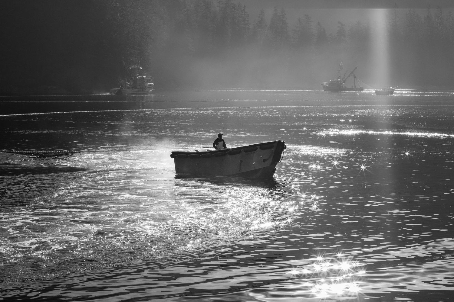 Black and white photo of a lone fisherman rowing a small boat across shimmering misty waters.