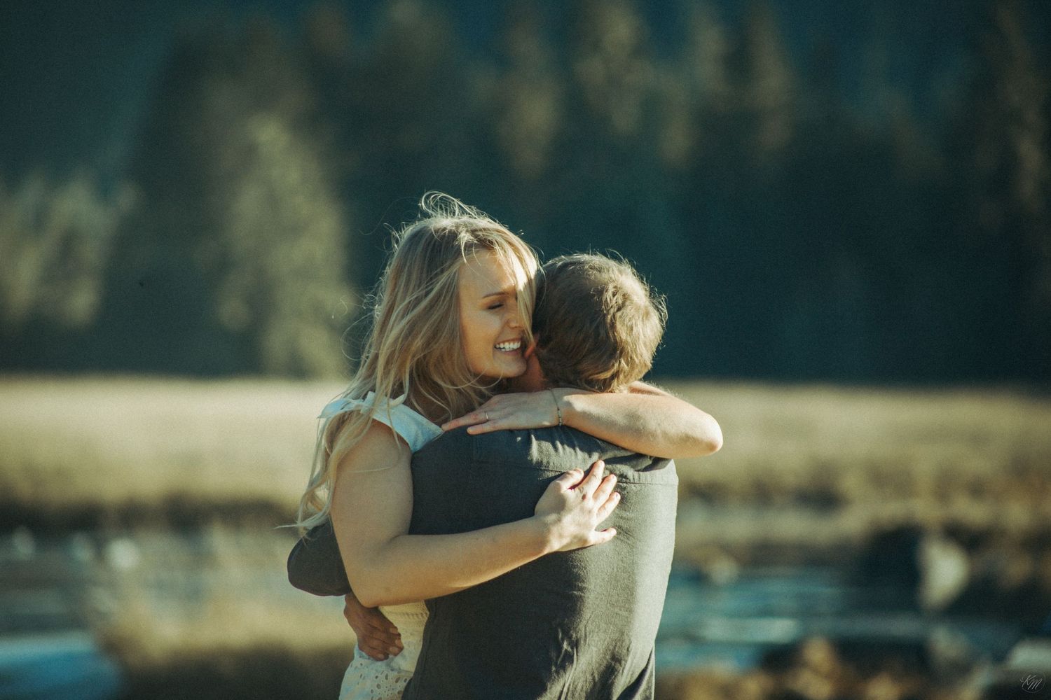 Intimate couple embracing near a peaceful lake during golden hour with trees in the background in Southeast Alaska.
