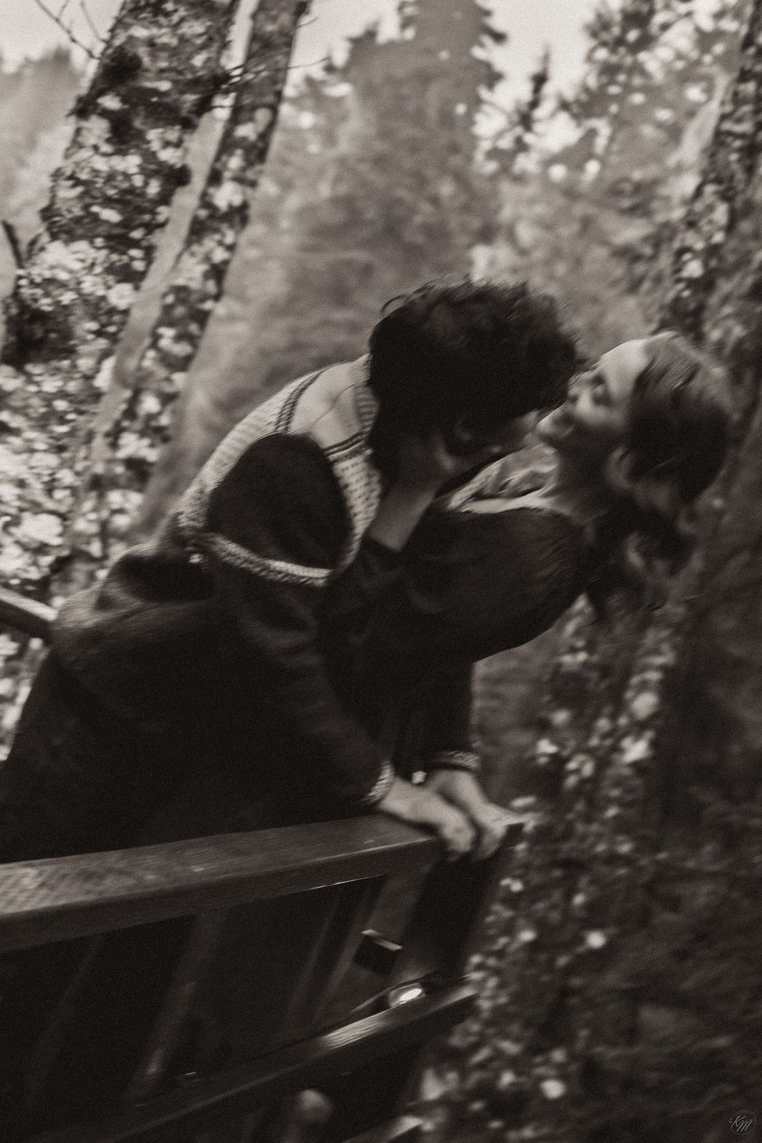 A romantic black and white photograph of a couple embracing on a bench in a wooded forest setting in Southeast Alaska.