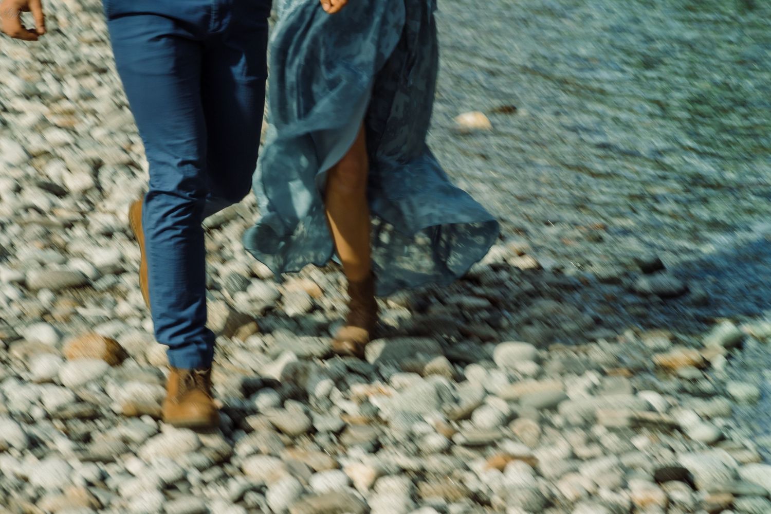 Close-up of couple's feet walking together on rocky riverbank.