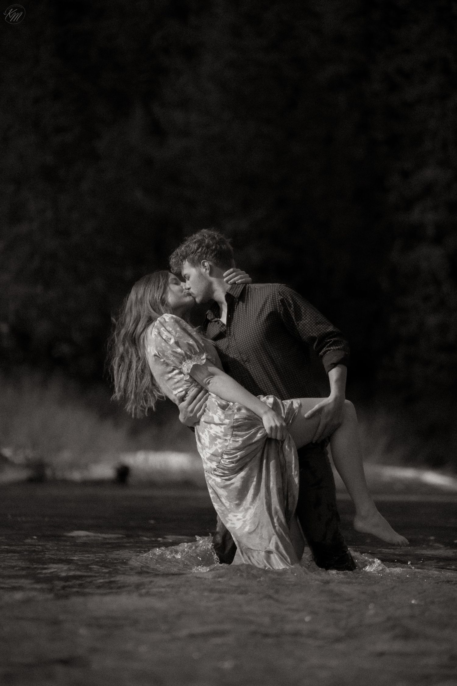 Dramatic black and white photos of couple sitting by water's edge.