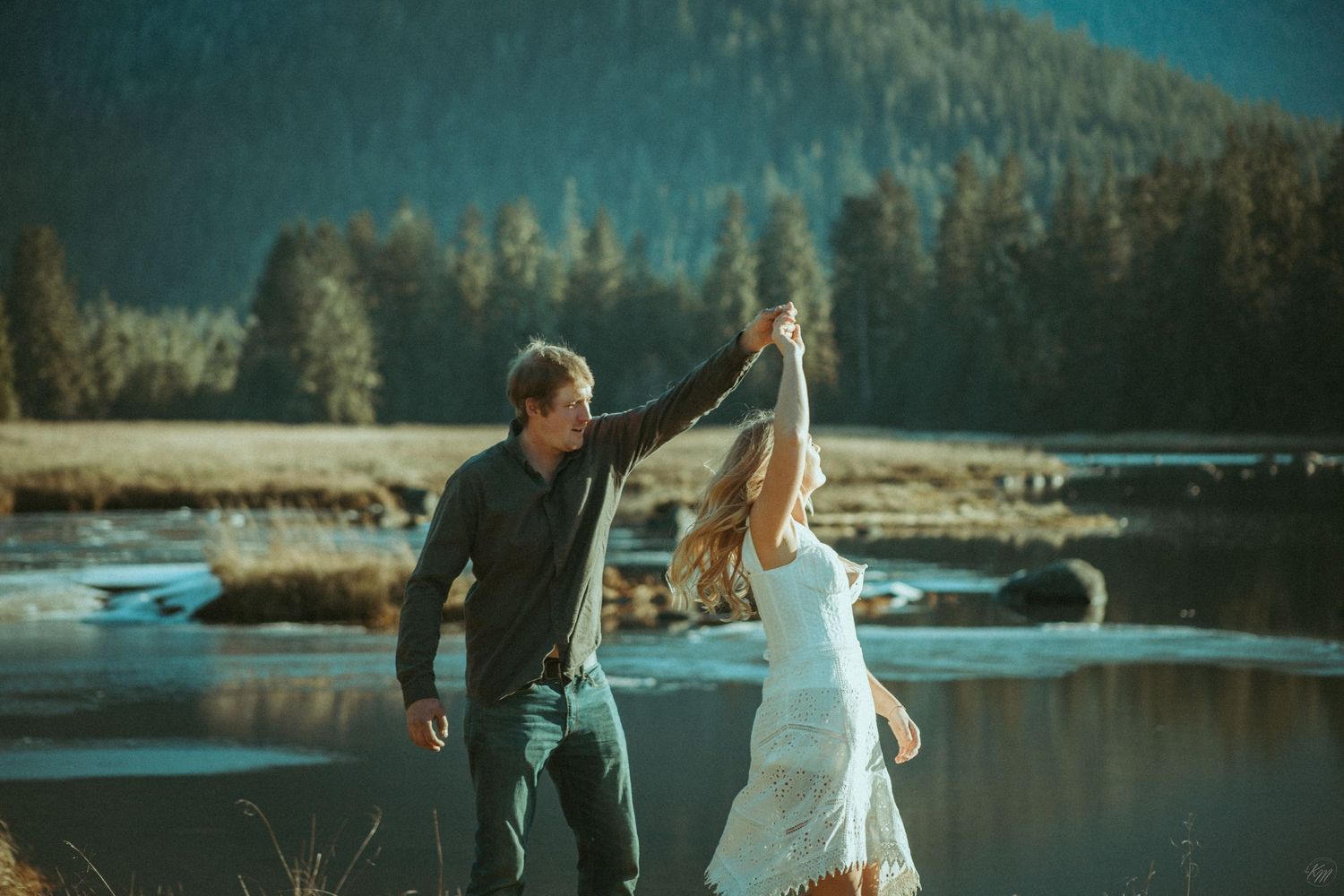 A couple in elegant attire dancing and twirling by a scenic mountain lake during sunset in Southeast Alaska
