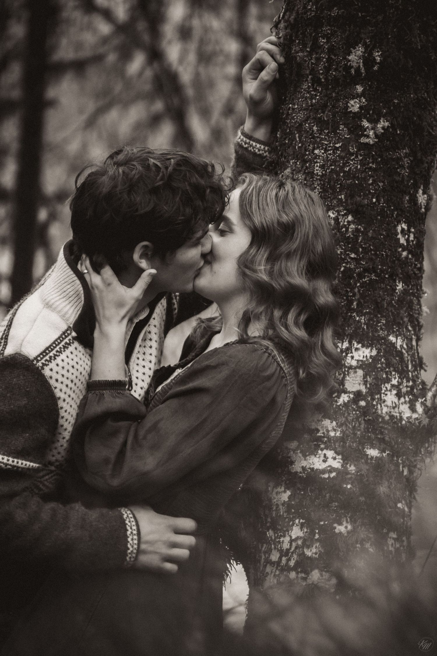 A romantic vintage black and white photograph of a couple kissing against a tree in a dreamy forest setting in Southeast Alaska.