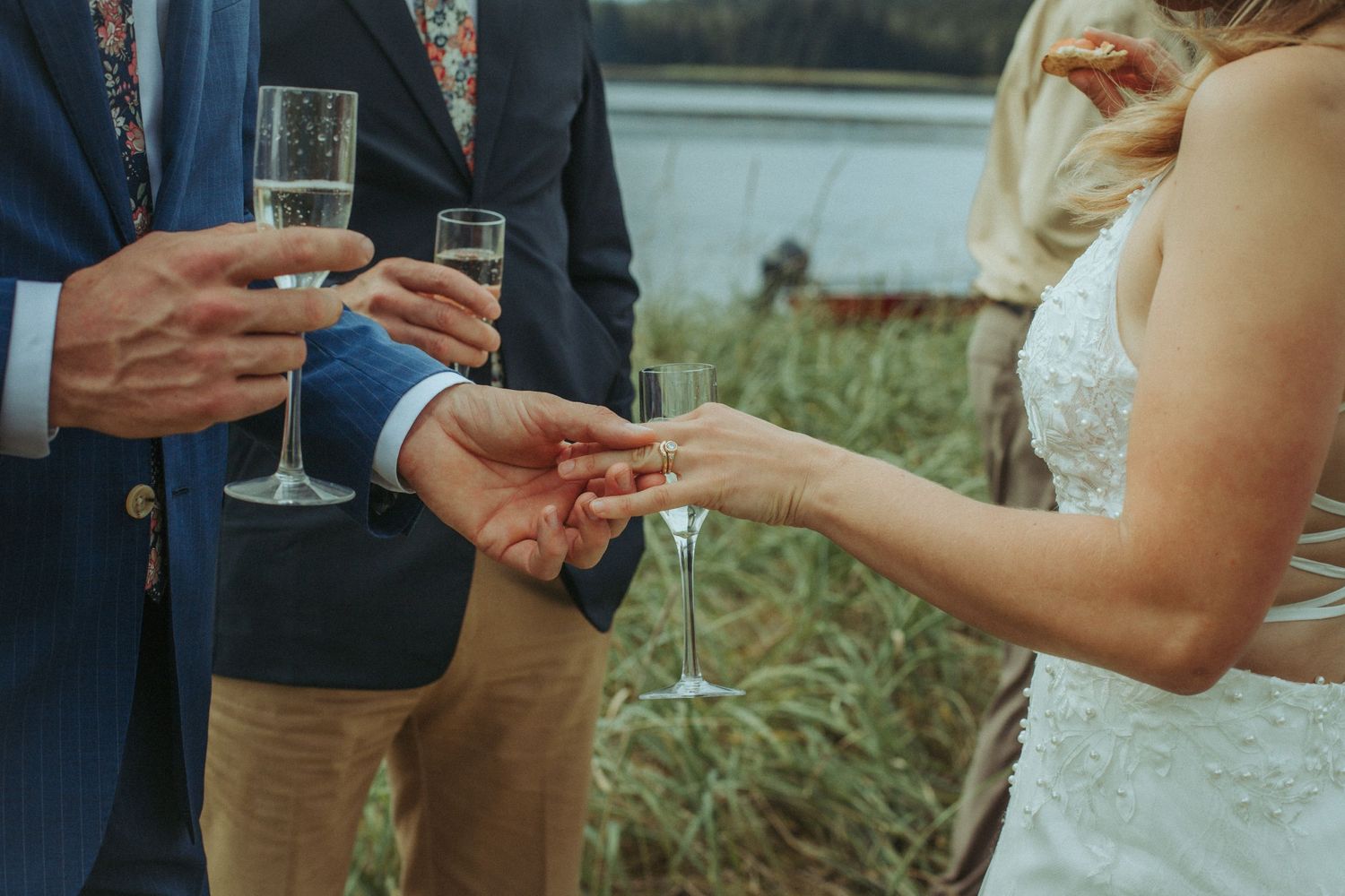 Close-up of hands exchanging rings during an outdoor wedding ceremony.