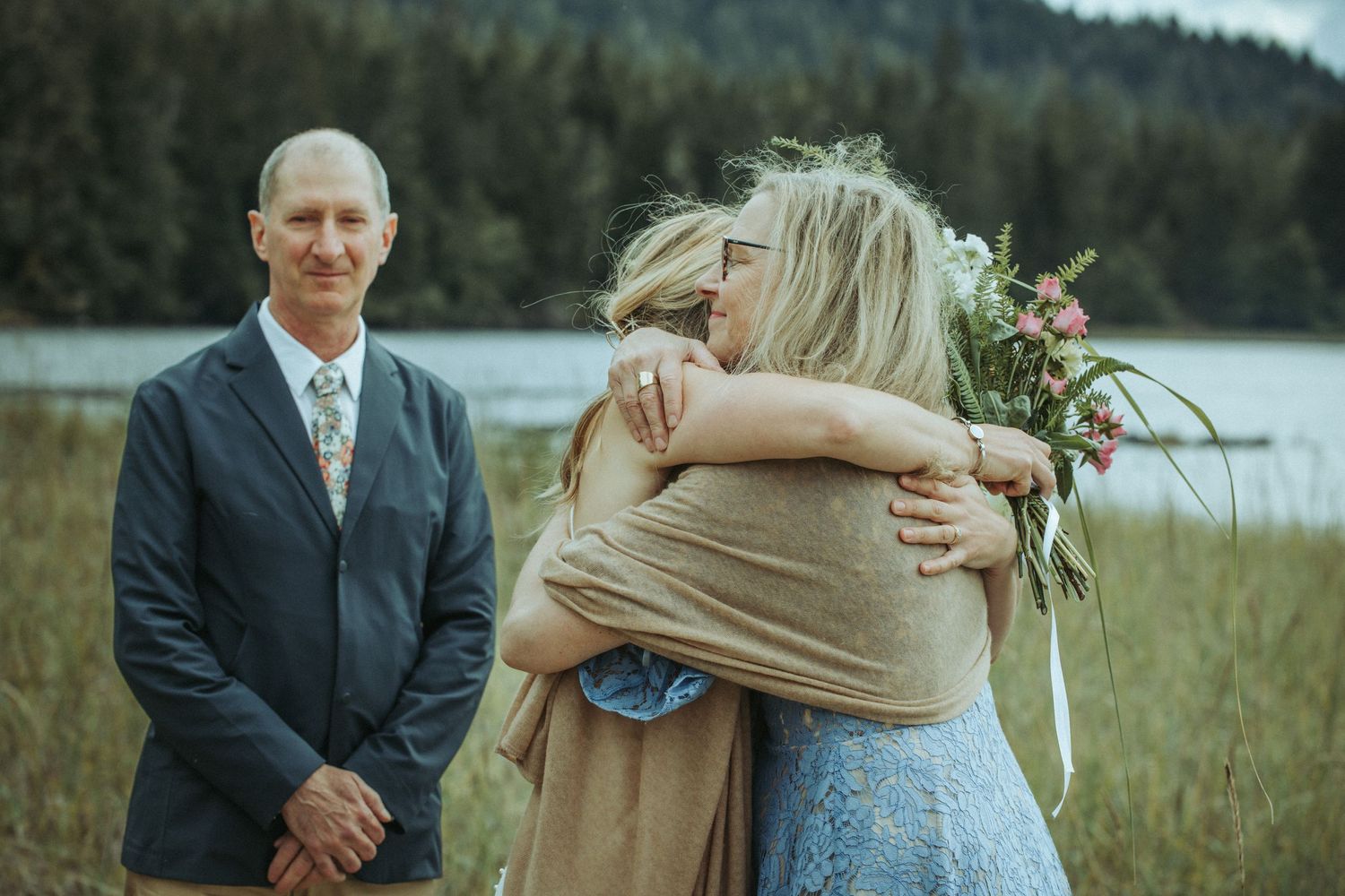 People share emotional moments during oceanside ceremony with mountain backdrop in Alaska.