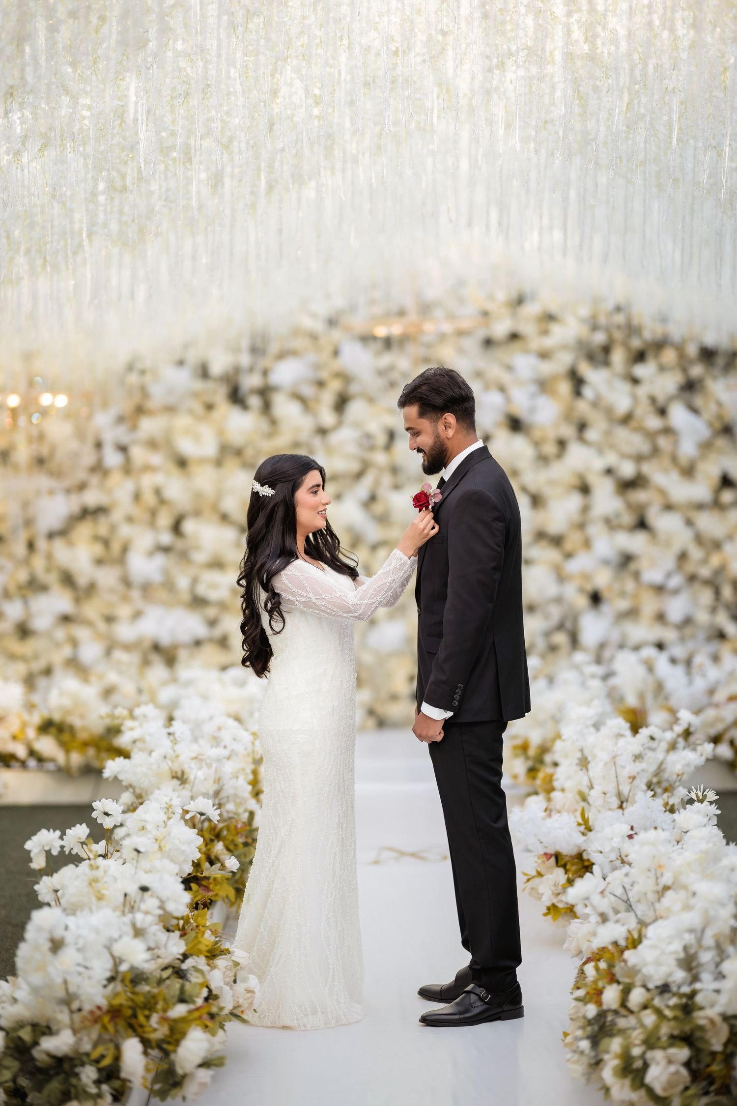 Wedding couple shares intimate moment surrounded by white floral arrangements and golden decor.