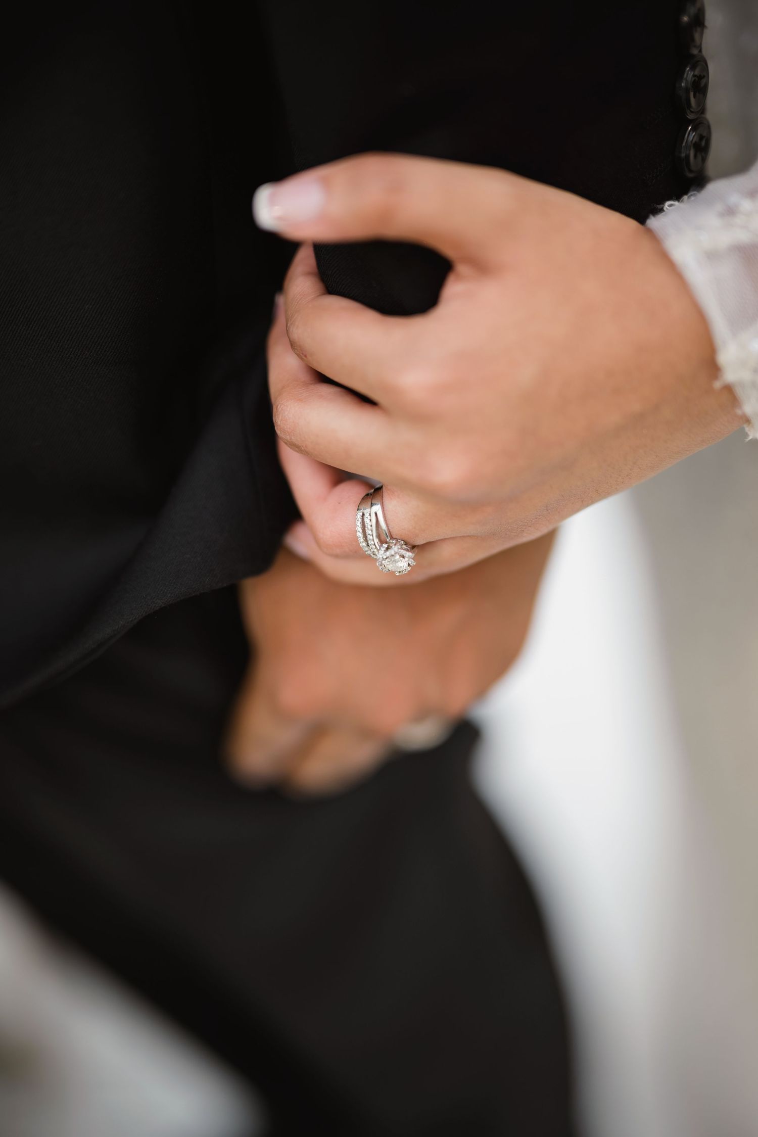 Close-up detail shot of hands wearing wedding rings against black and white formal attire.