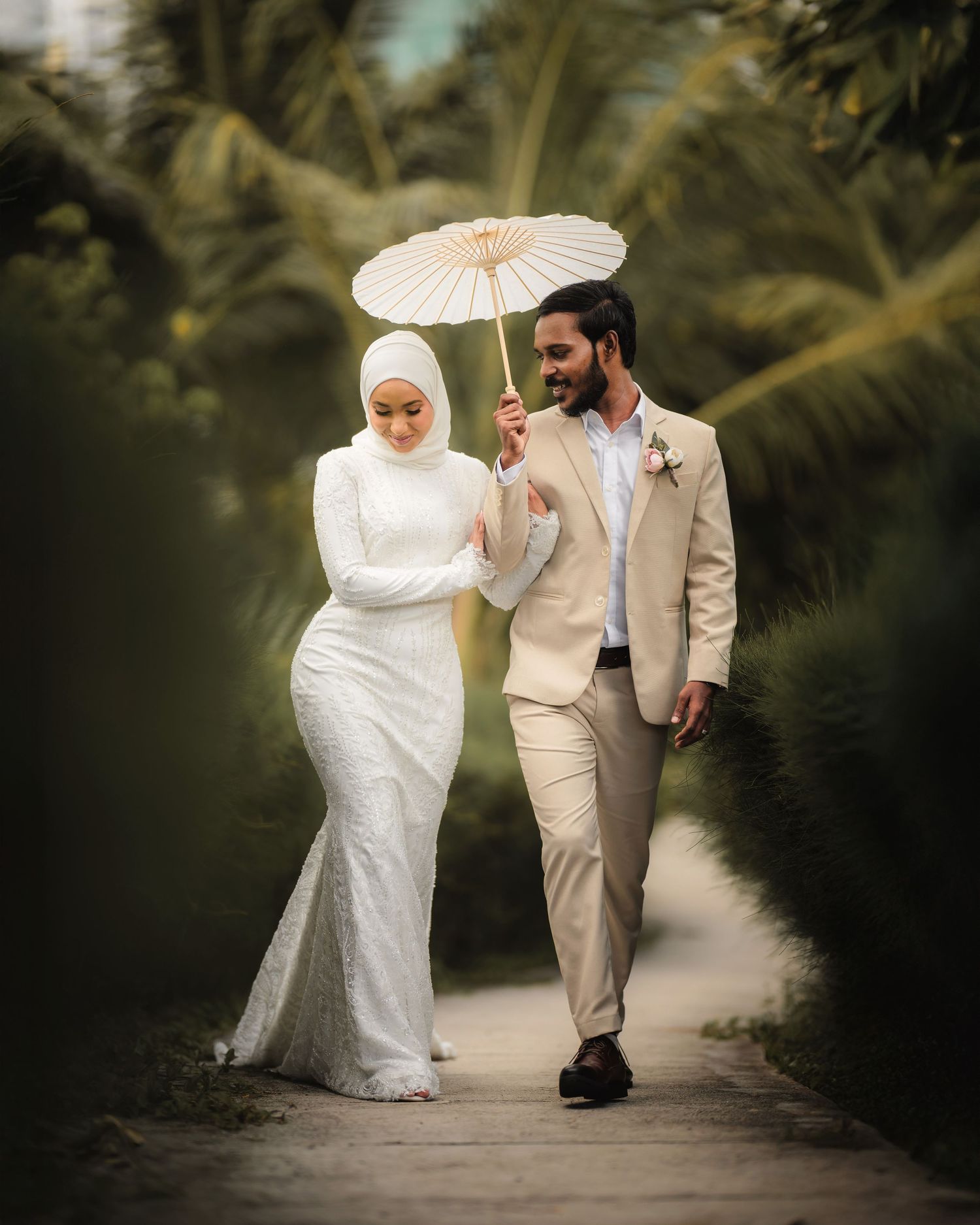 A couple walks along a palm-lined path carrying white parasols.