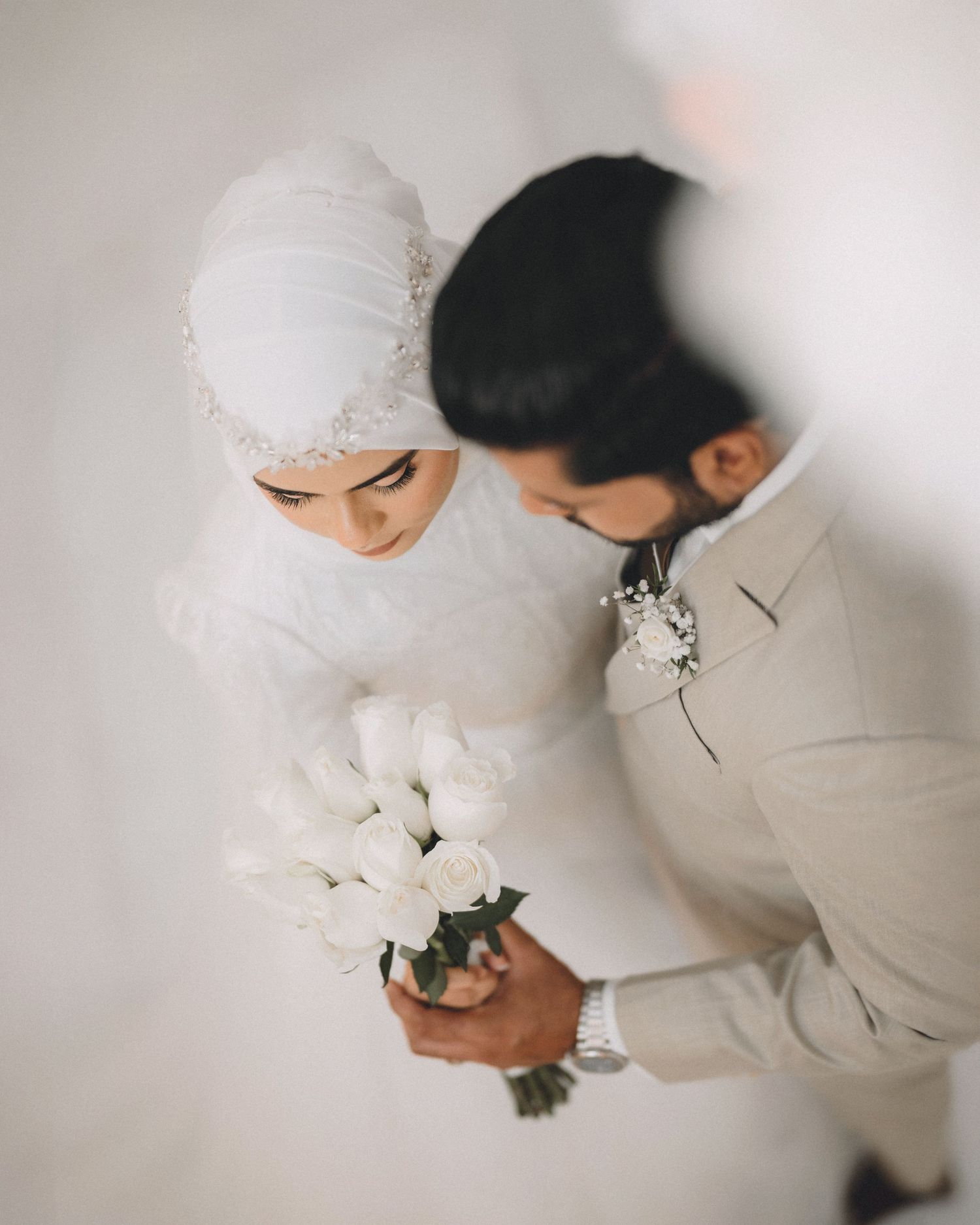 Elegant couple in white attire share intimate moment during wedding photoshoot.
