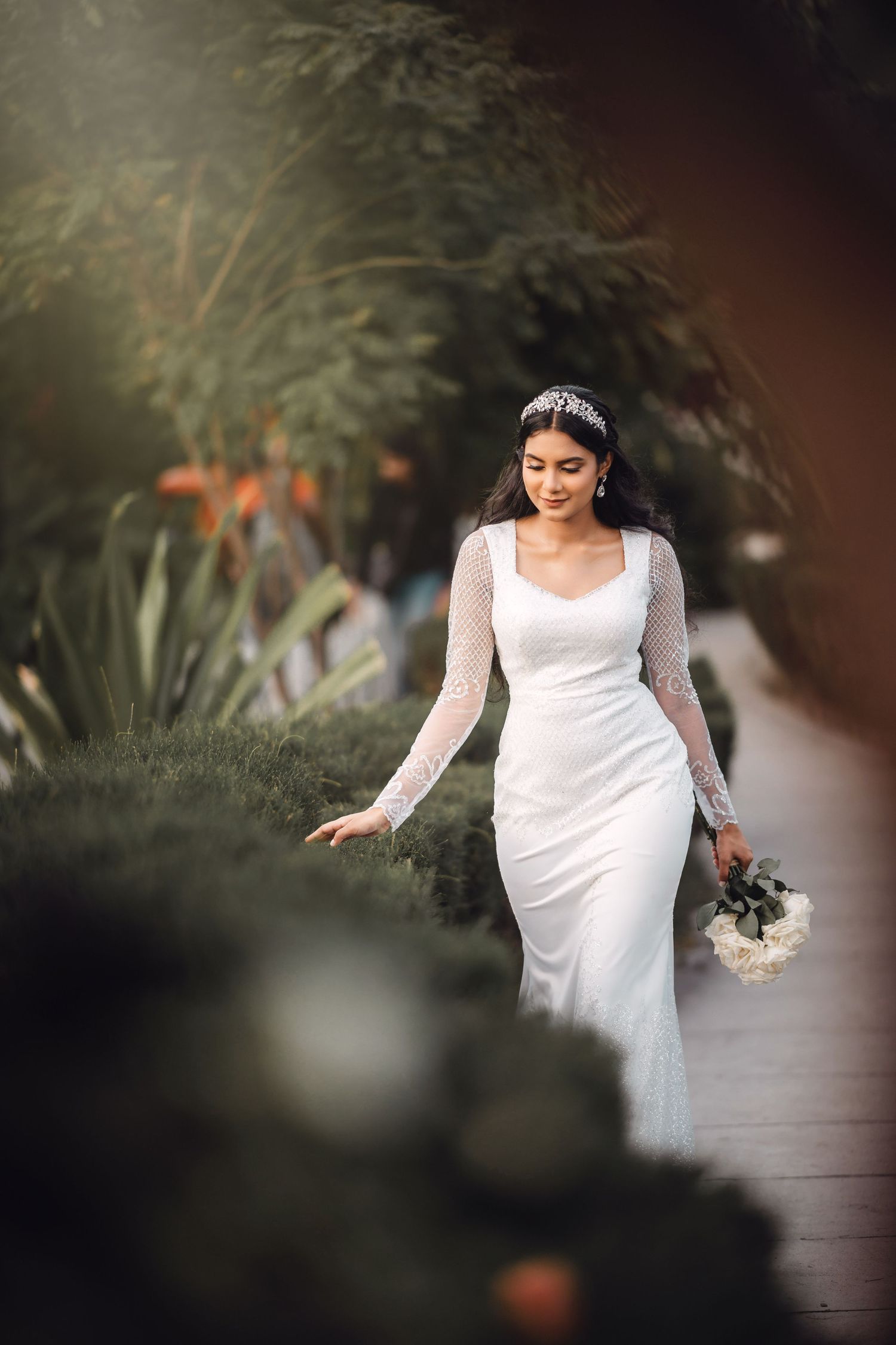A bride in a flowing white dress walks through a lush garden setting.