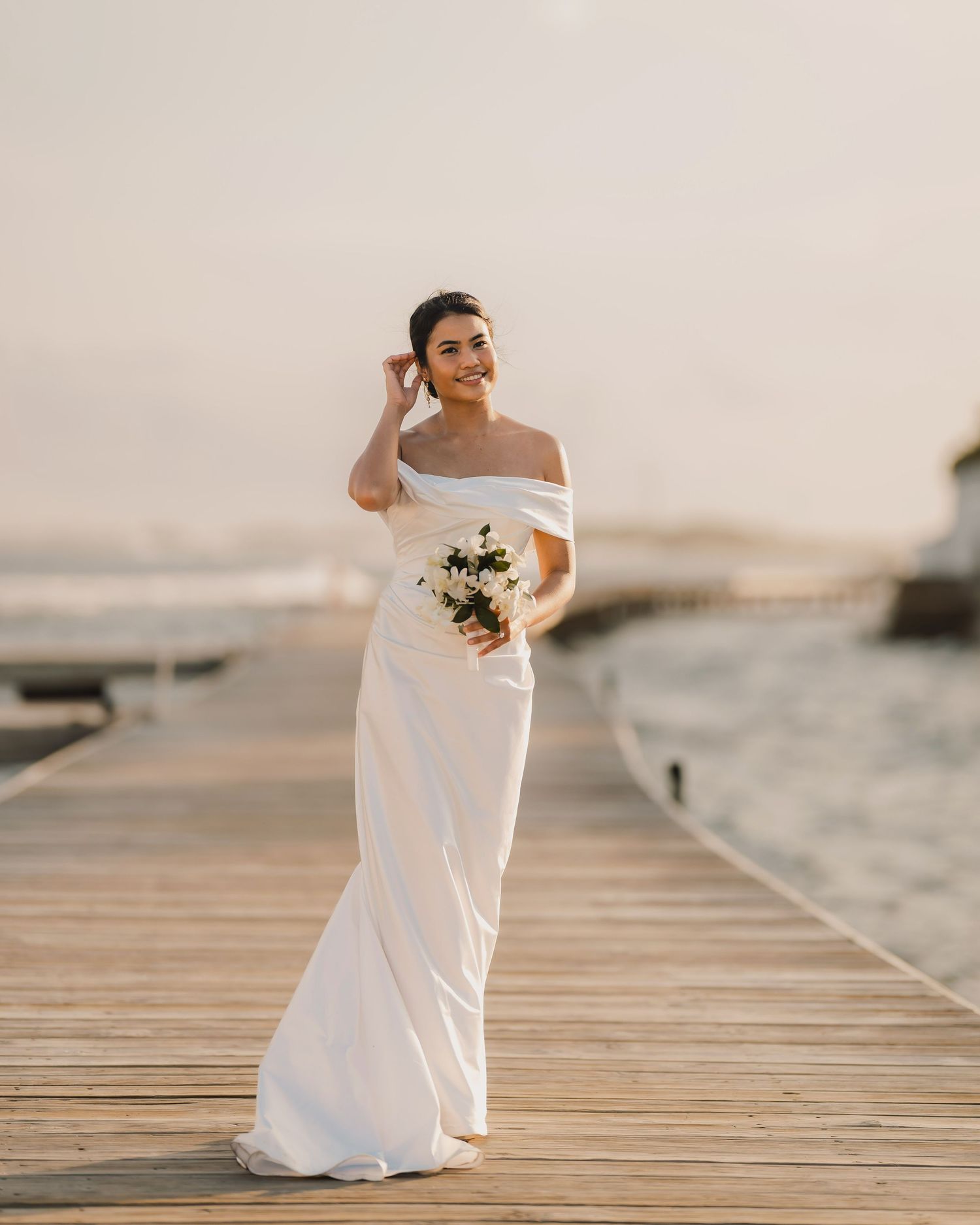 Elegant white wedding dress photographed in sequence on a wooden dock at sunset.